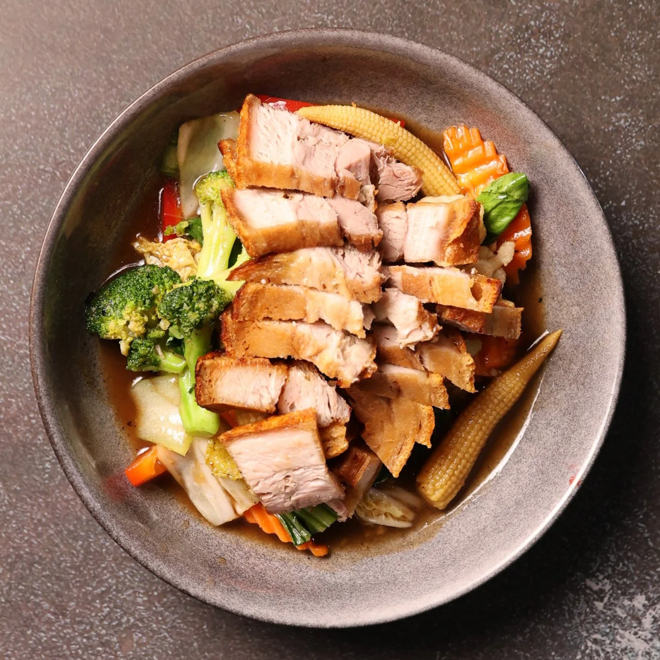 A bowl of Asian stir-fry with fried chicken, broccoli, baby corn, carrots, and other vegetables in a savory sauce.