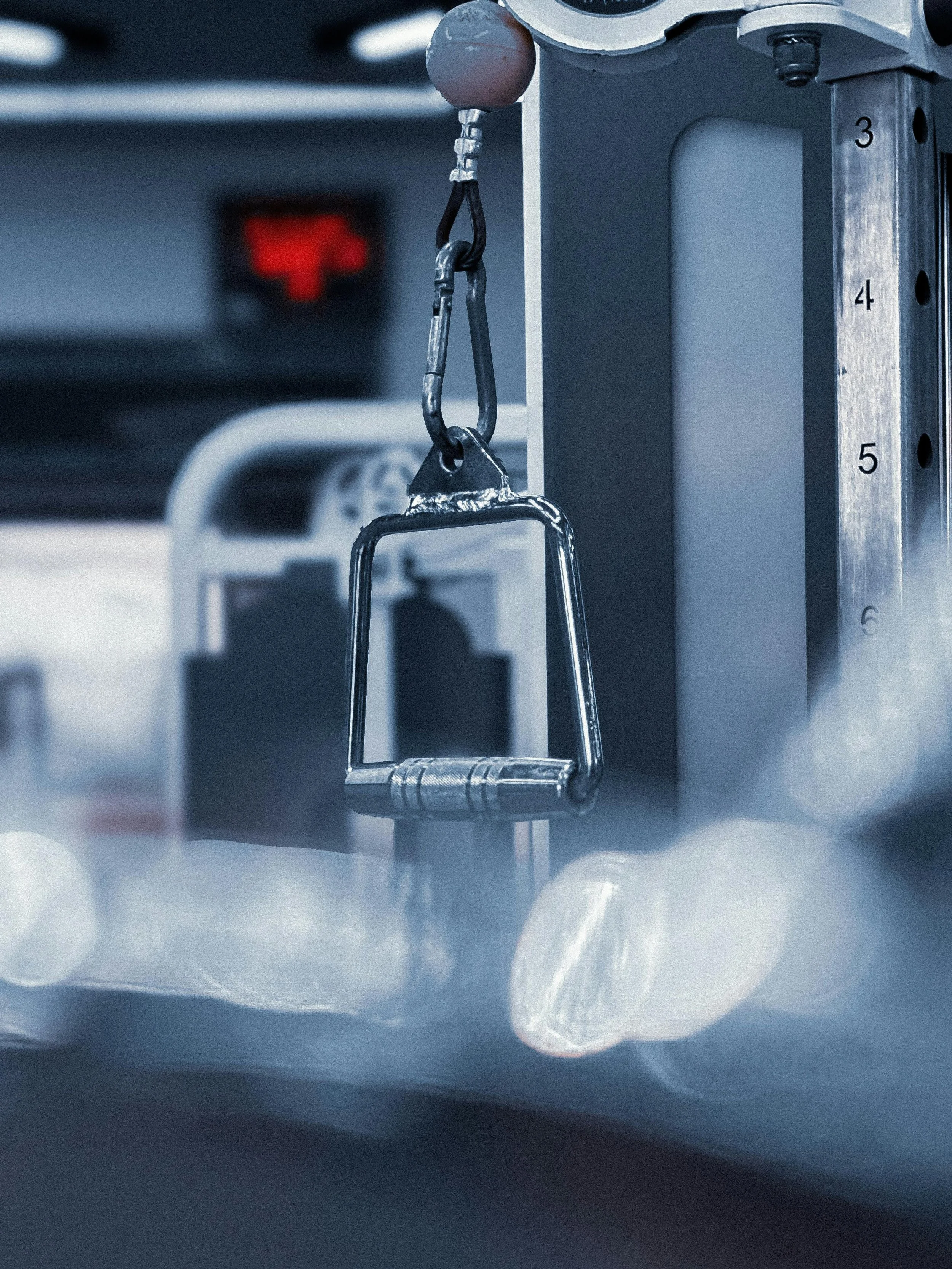 A set of handles hanging from a cable machine with a blurred foreground of other gym equipment.