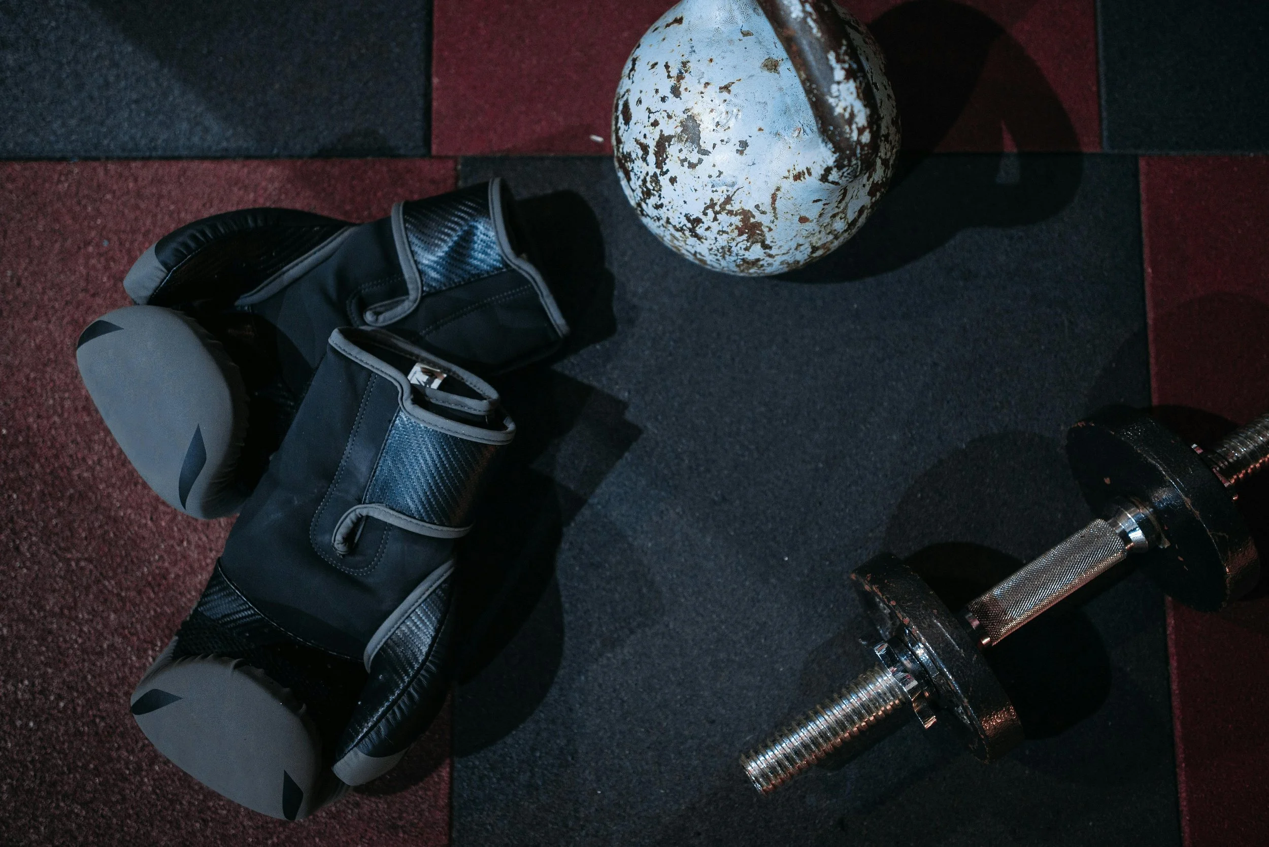 A golf bag with clubs, a rusty golf ball washer, and a golf club on a foam mat surface at a golf course or driving range.