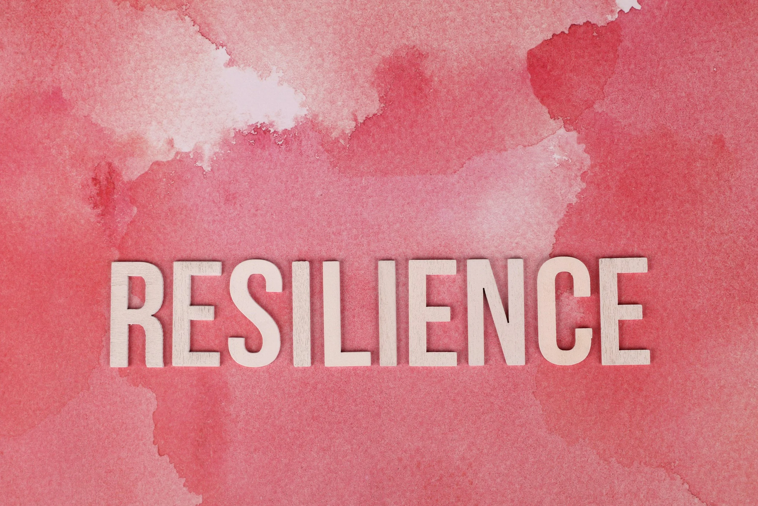 Pink watercolor background with white wooden letters spelling 'RESILIENCE' at the bottom.