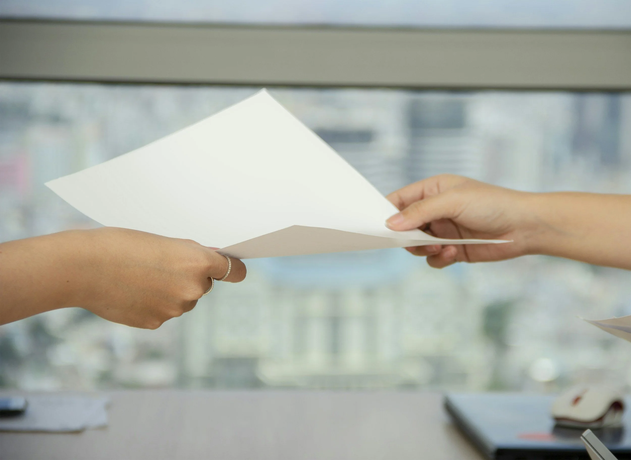 Close-up of hands exchanging a white piece of paper in an indoor setting with a blurred background.