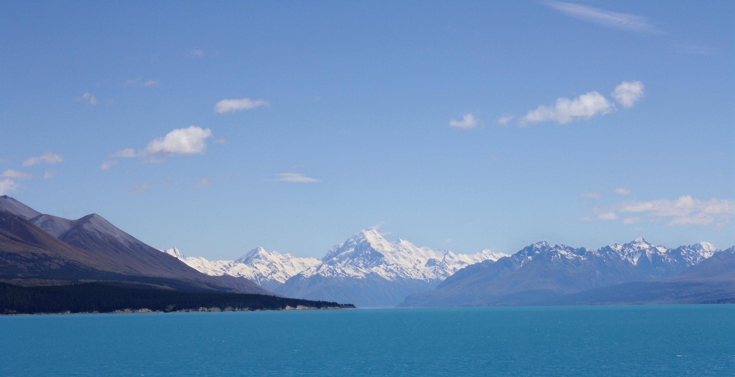 Snow-capped mountains with a blue lake in the foreground under a clear blue sky.
