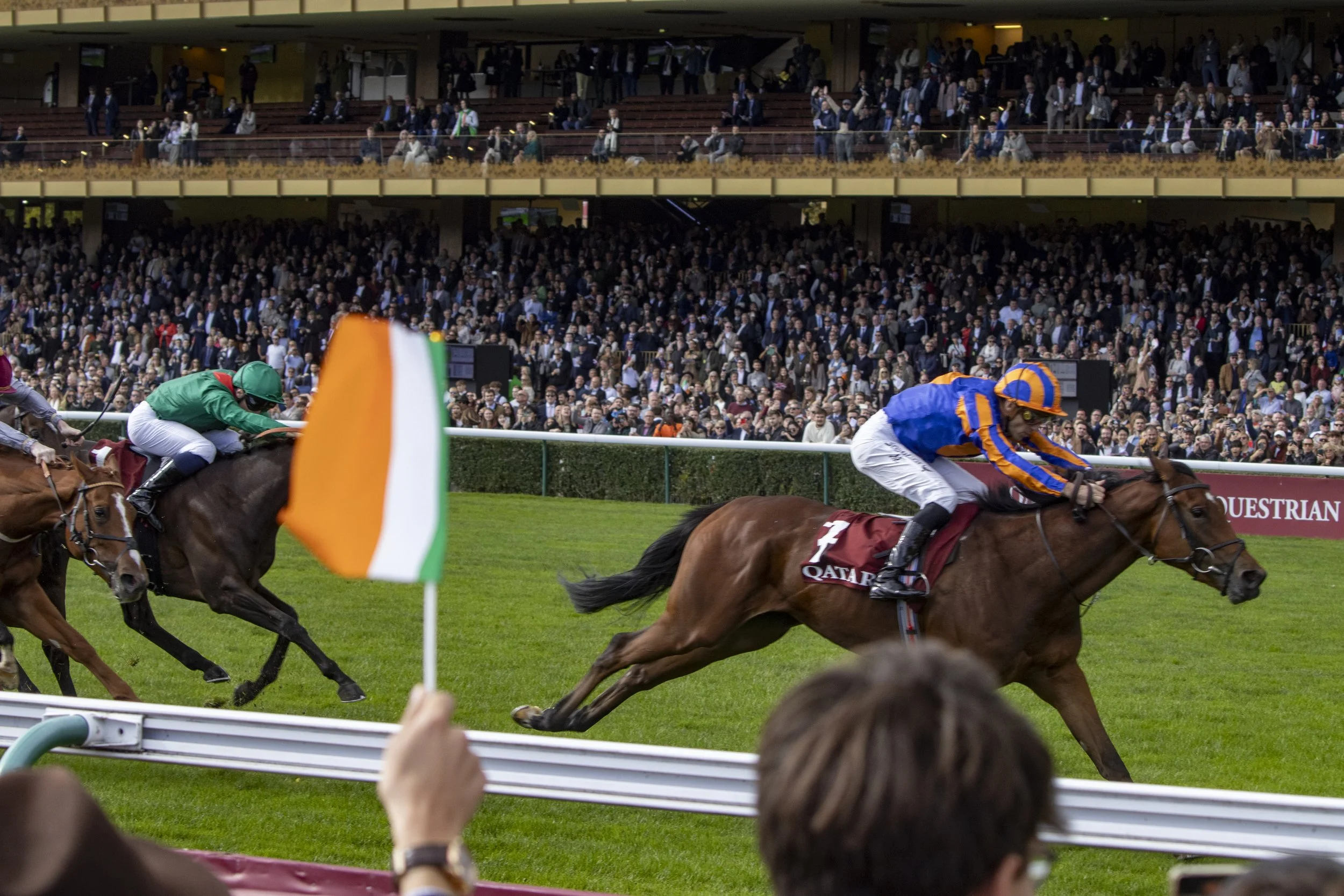 Jockeys riding horses in a race with a crowd of spectators in the background.