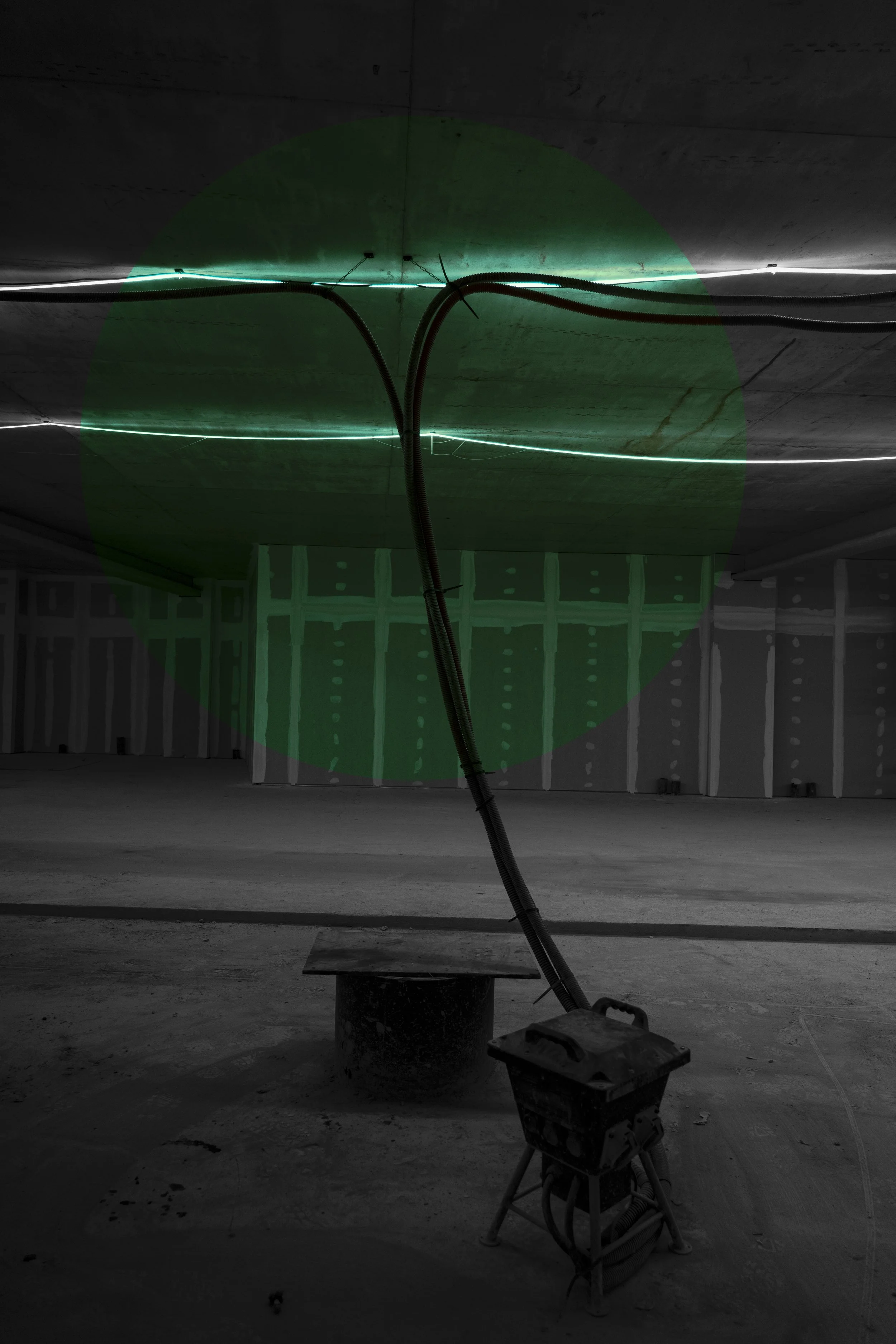 Underground parking garage with construction materials and tools, including a bright green laser line and electrical cables hanging from the ceiling.