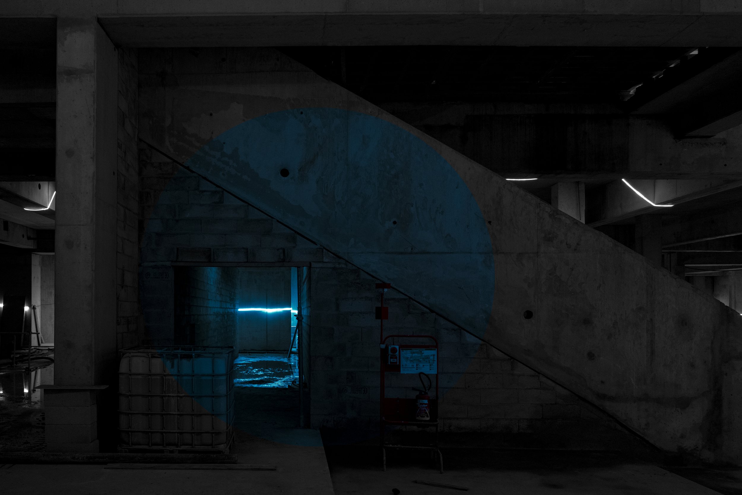 An underground parking garage with concrete structure and minimal lighting, featuring blue accent lights and construction equipment.