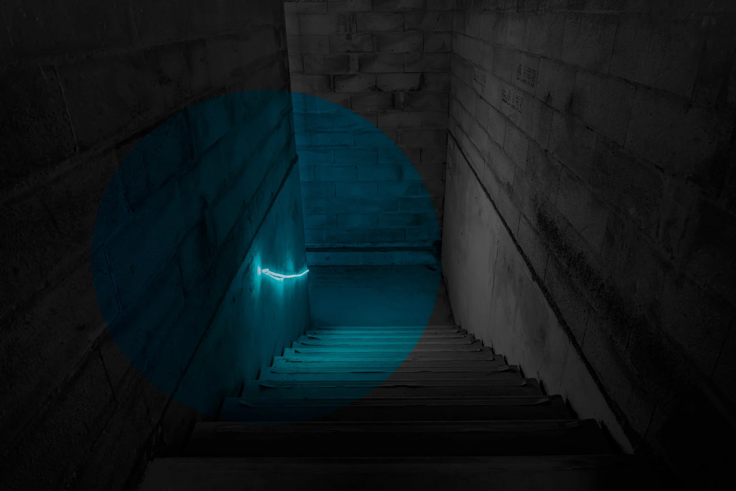 A dark staircase with concrete walls illuminated by blue LED lighting, descending into a mysterious area.