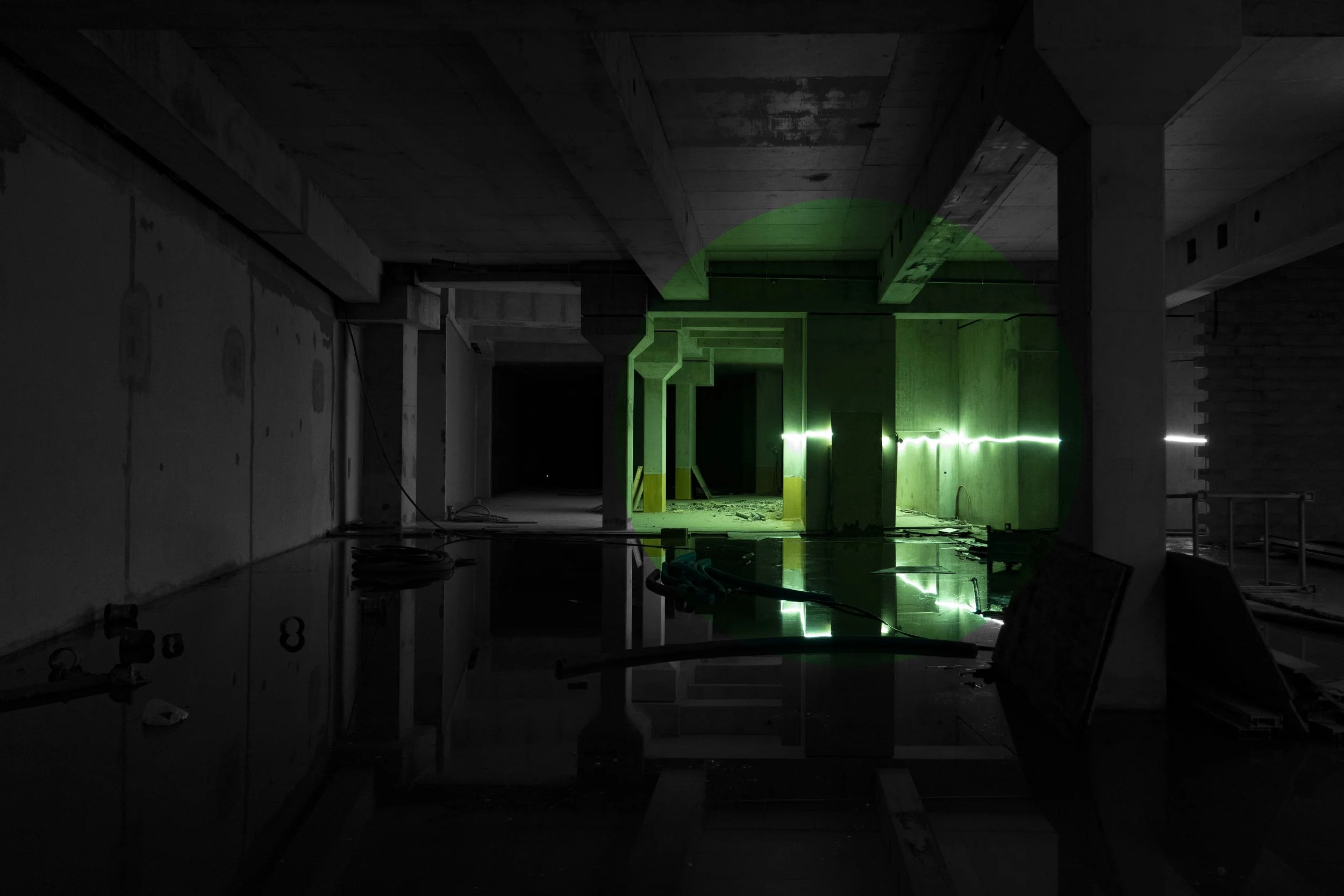 Dark indoor construction site with green laser line and reflections on a floor.