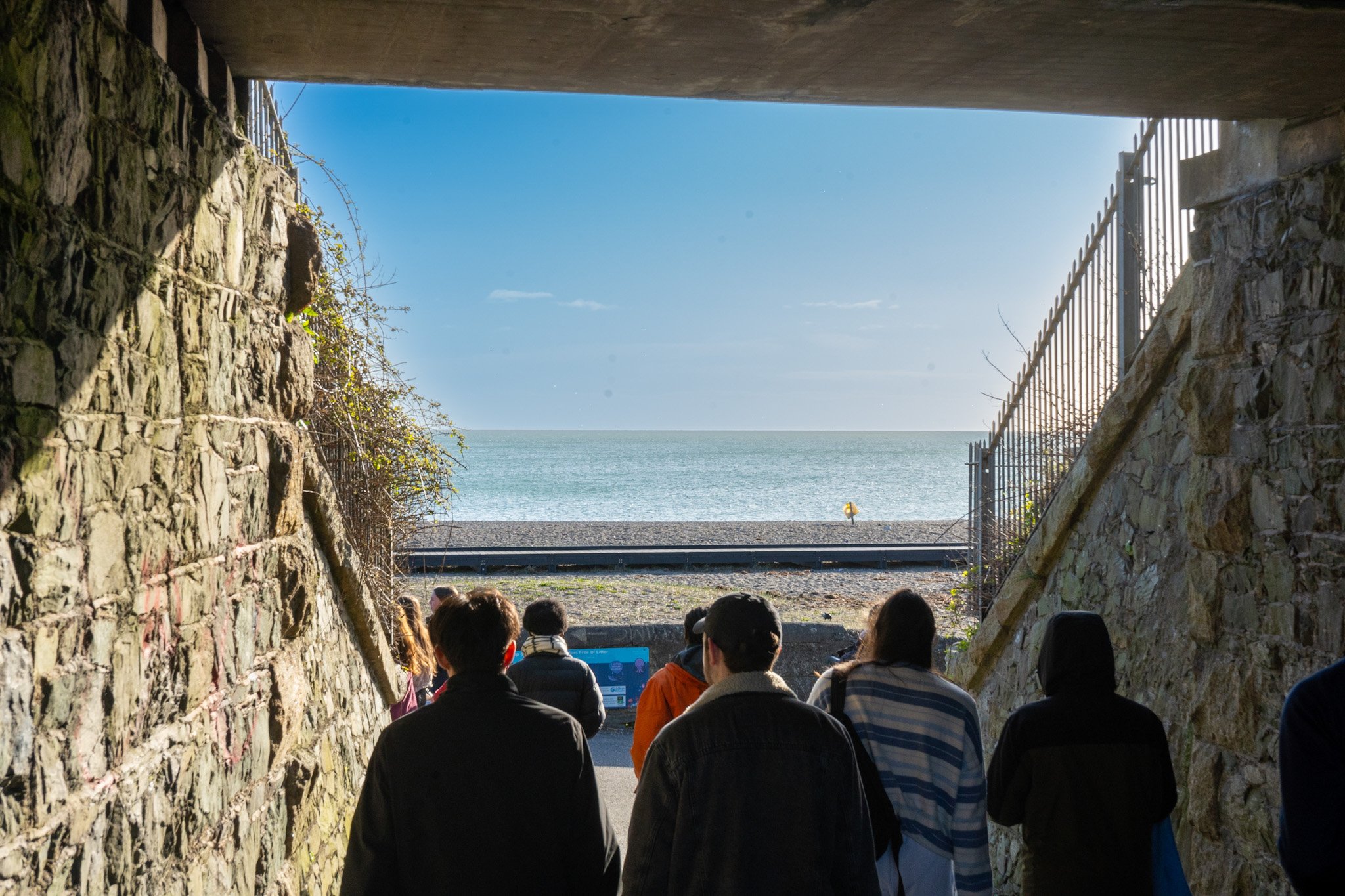 People sitting under a tunnel looking out at the ocean and sky.