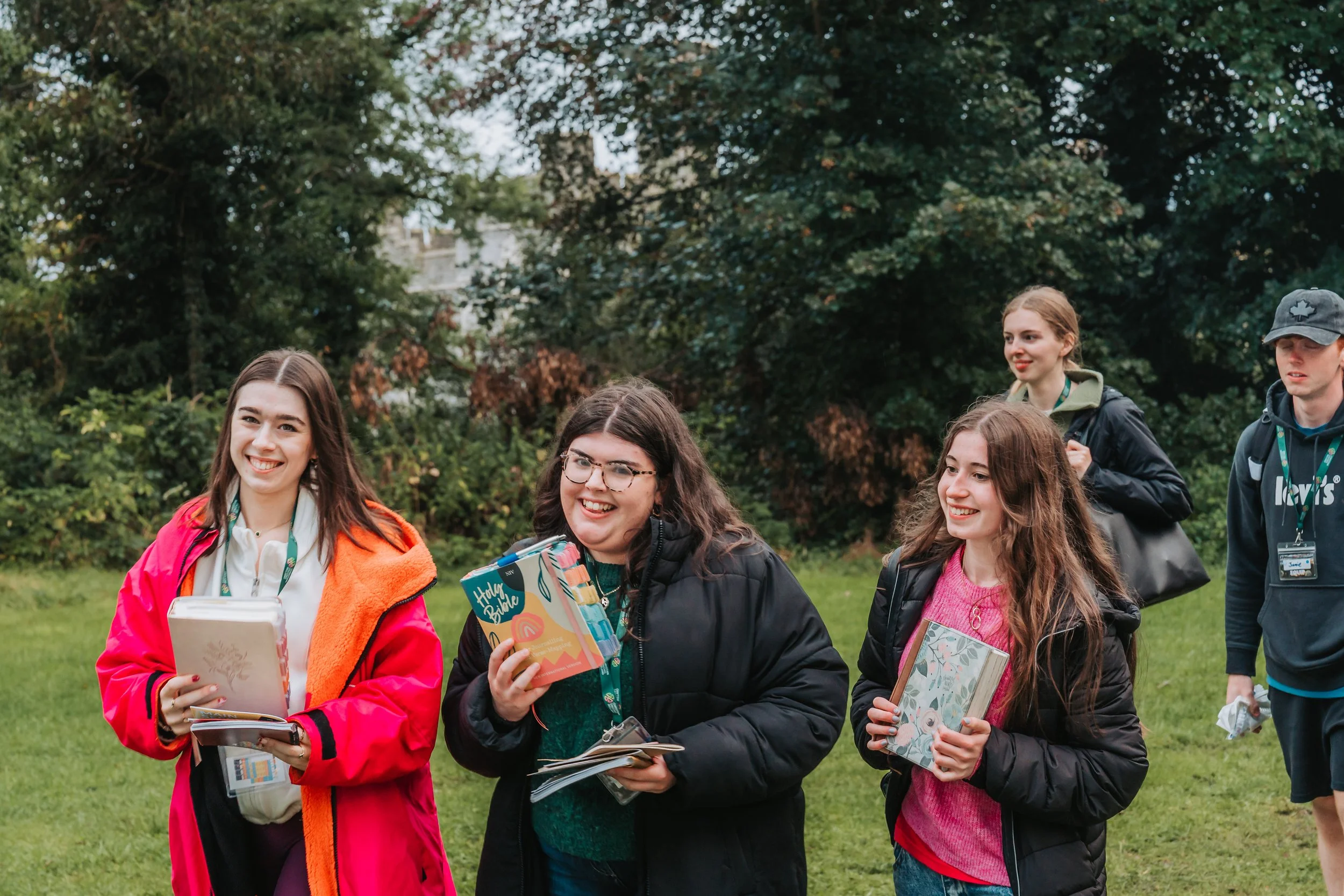A group of young people outdoors, holding books and smiling, with trees in the background.