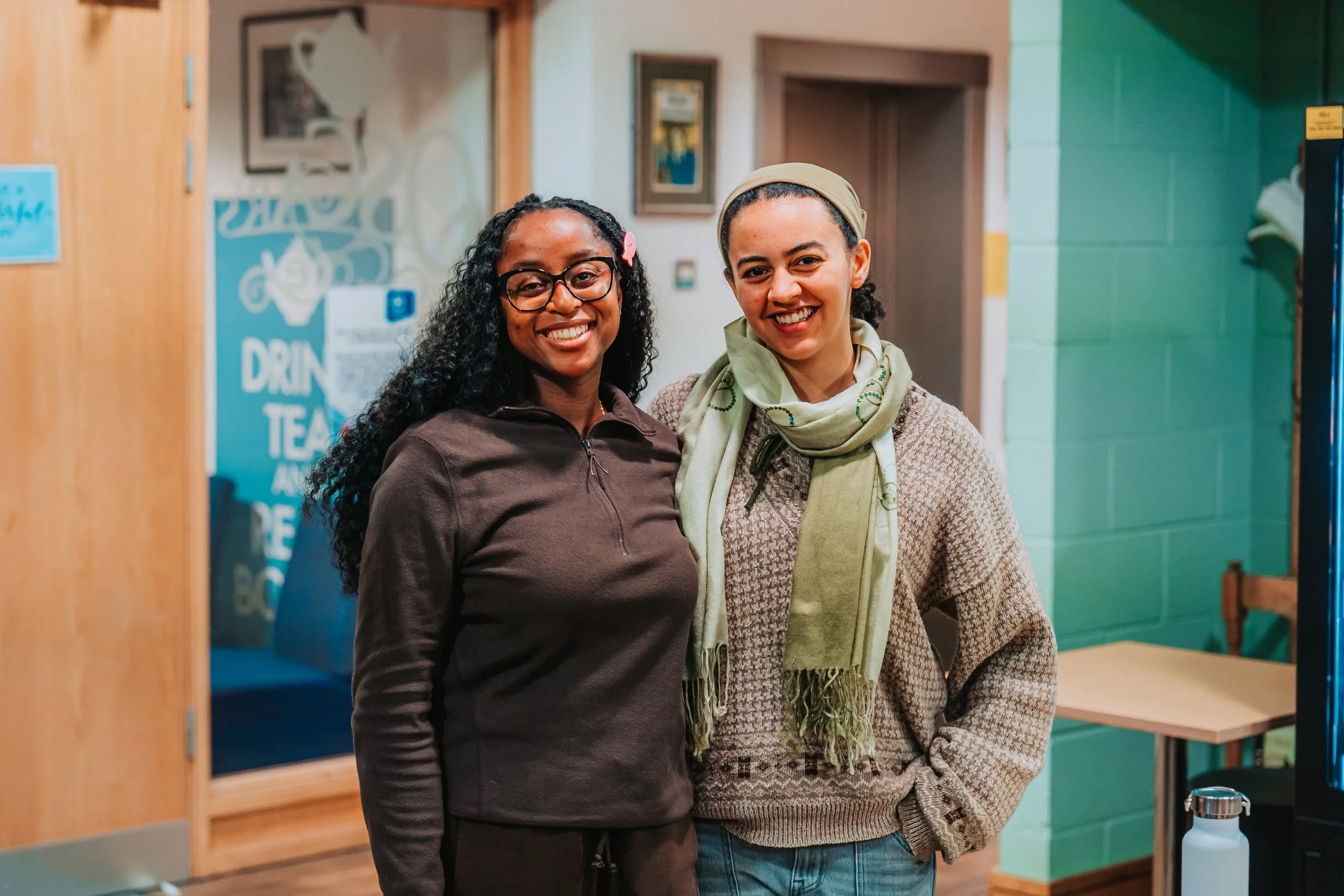 Two women standing together indoors, smiling at the camera.