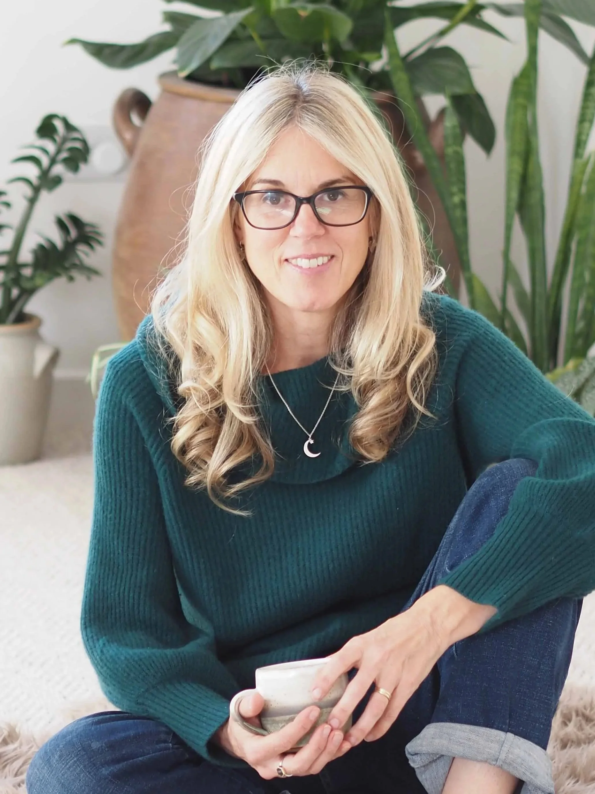 photo of claire branigan white middle aged woman wearing green jumper in wellbeing studio surrounded by plants and nature elements