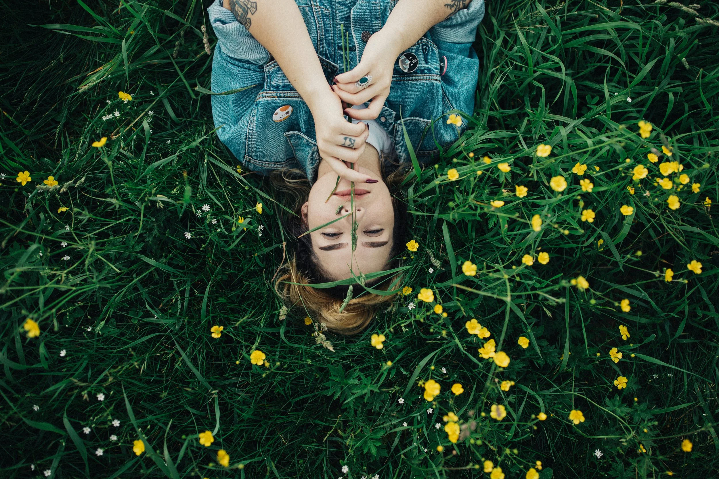 photo of a young white woman lying down in a meadow looking calm and peaceful enjoying an econidra nature meditation session