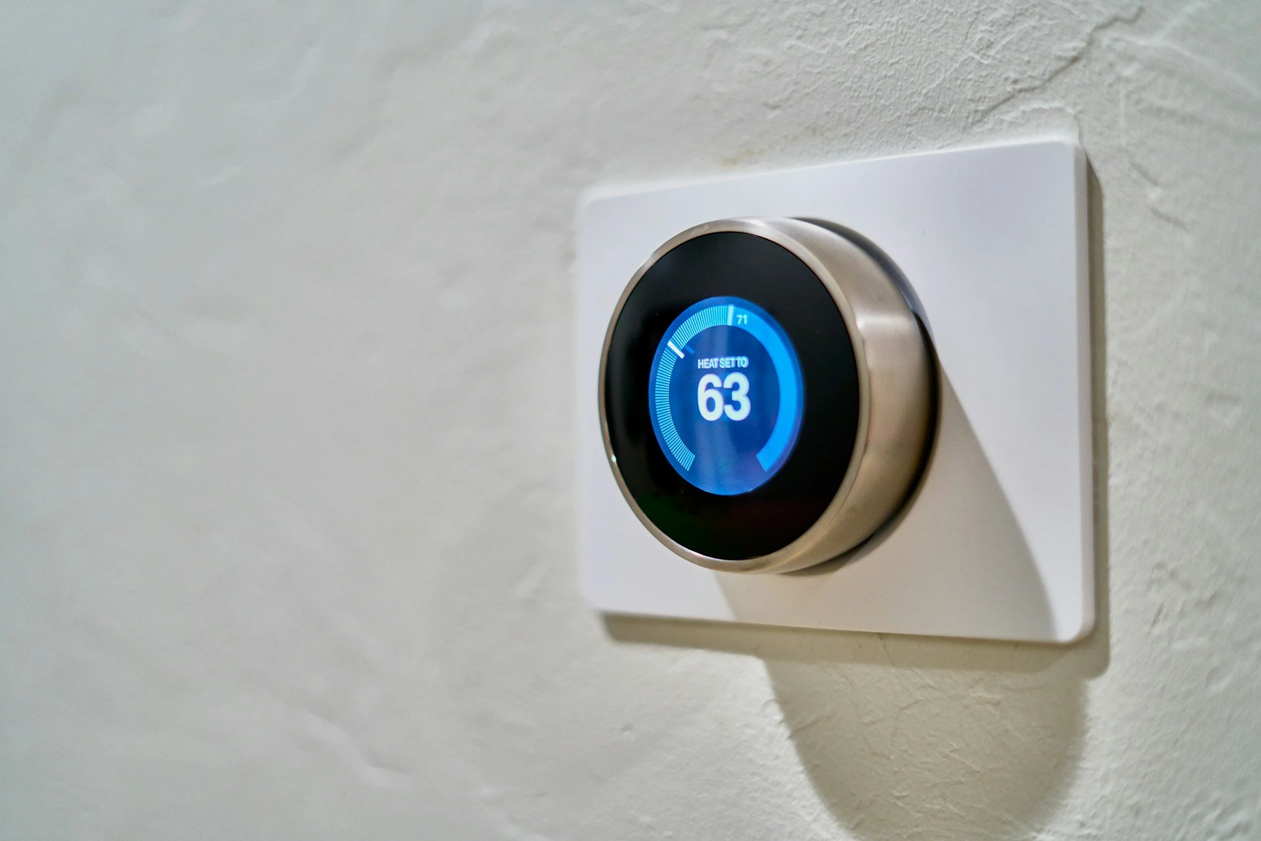 Smart thermostat on a white wall displaying a temperature of 63 degrees Fahrenheit.