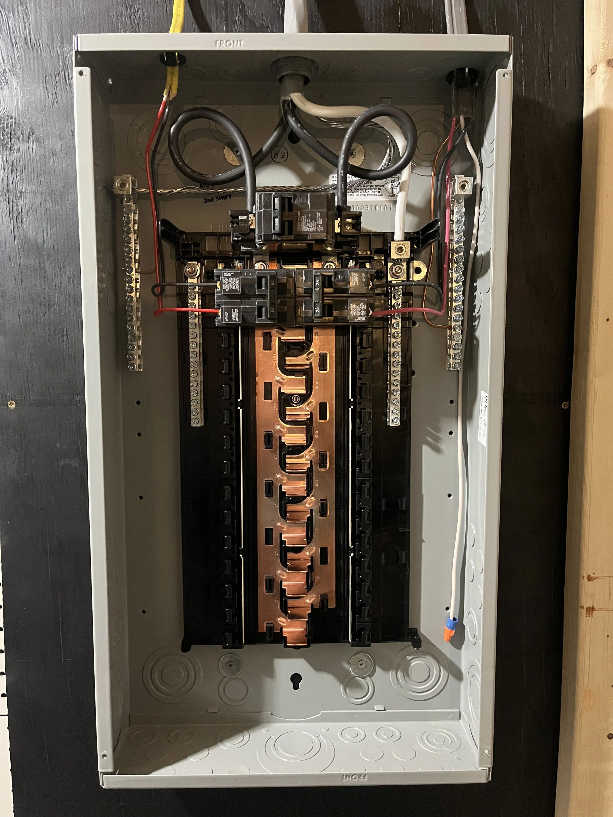 Open electrical breaker panel with multiple circuit breakers and wiring inside a gray metal box.