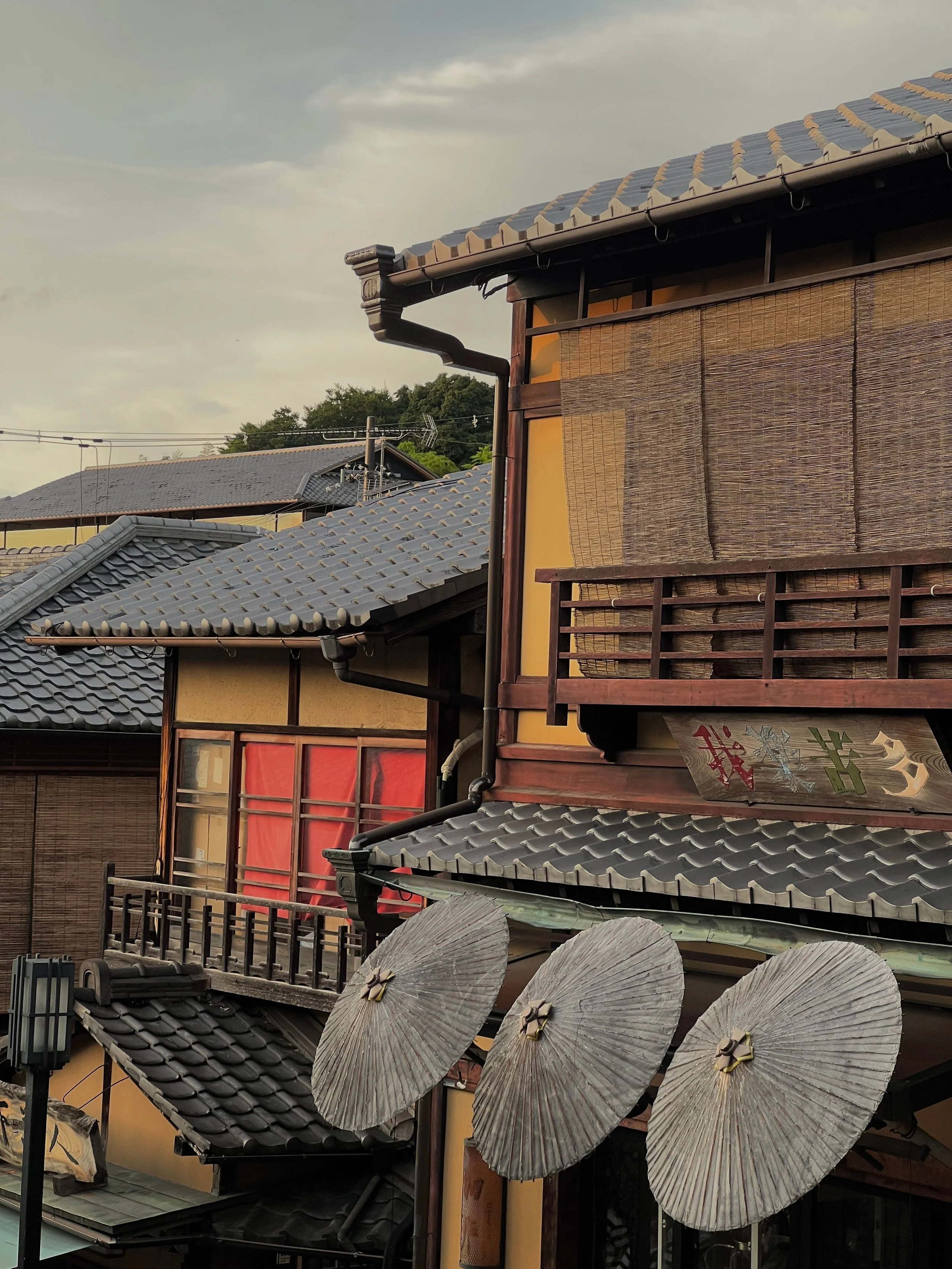 Traditional Japanese building with tiled roof, bamboo shades, paper umbrellas, and weathered paper lanterns outside