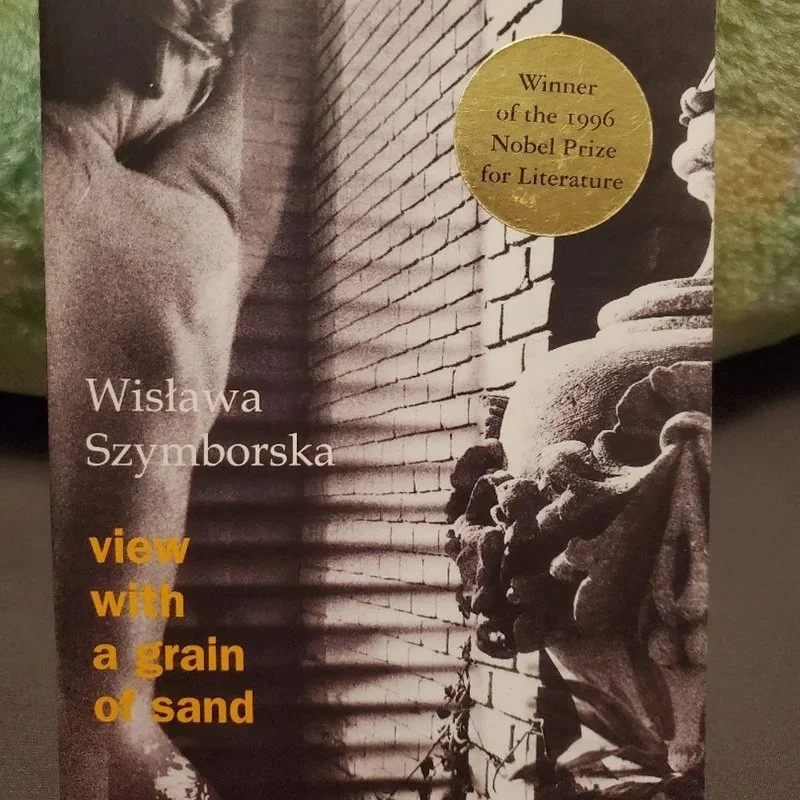 Book cover of 'View with a Grain of Sand' by Wisława Szymborska, featuring a black and white photograph of a woman near a brick wall and a classical sculpture with a gold sticker indicating she won the 1996 Nobel Prize in Literature.