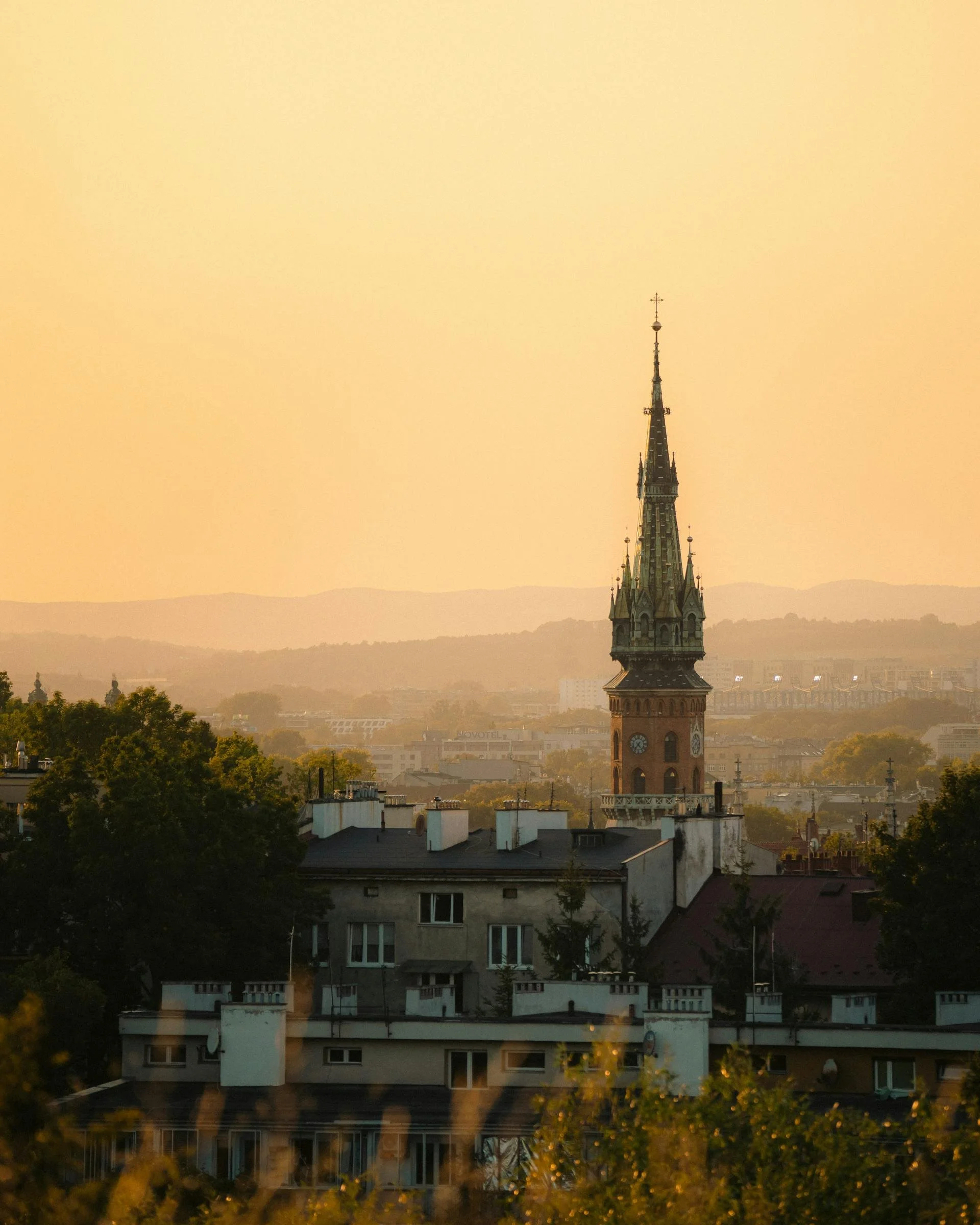 Utsikt over Kraków ved solnedgang med kirkespir og grønne trær.