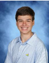 Young man with short dark hair, smiling, wearing a light blue collared shirt with a small yellow logo, against a blue cloudy background.