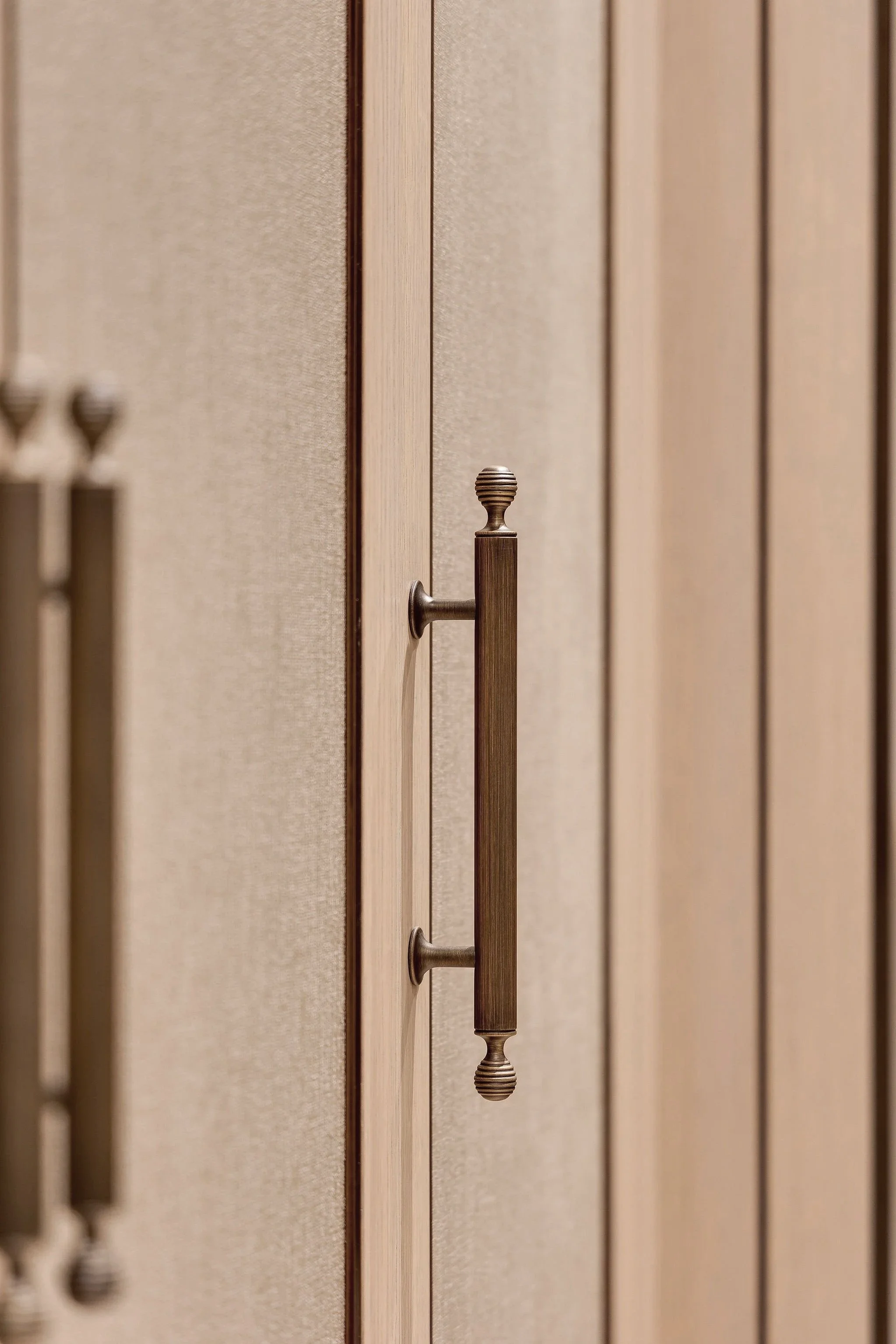 Close-up of wooden door handles mounted vertically on a textured beige wall.