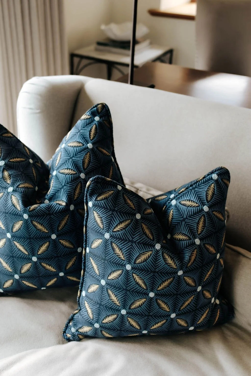 Close-up of two decorative pillows with a blue and gold leaf pattern on a beige sofa in a living room.