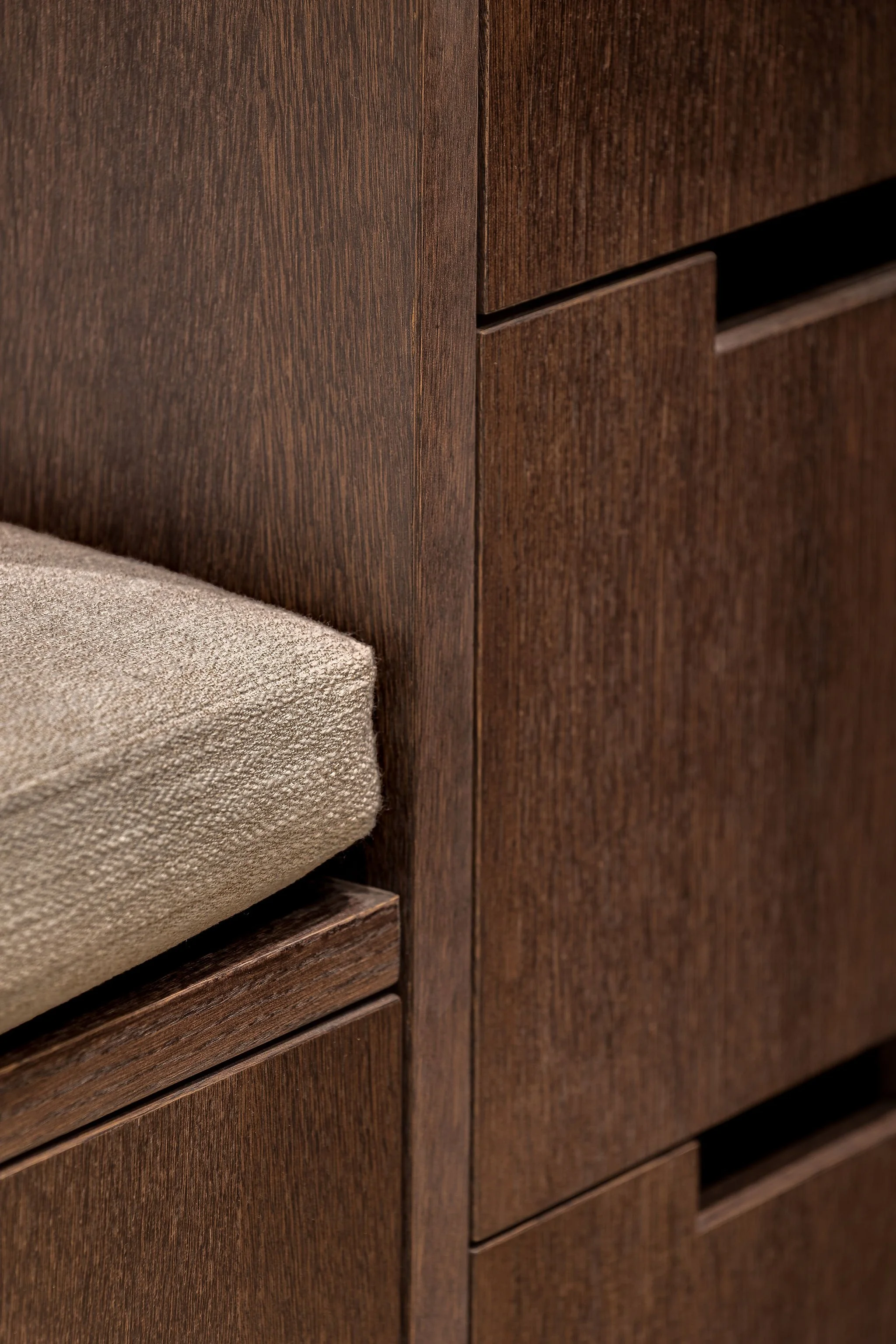 Close-up of a wooden cabinet with a beige upholstered cushion on a wooden stool in front.