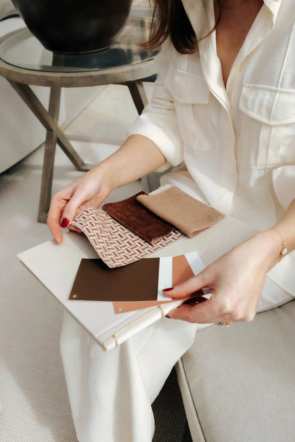 A woman sitting on a sofa reviewing fabric samples and color swatches.