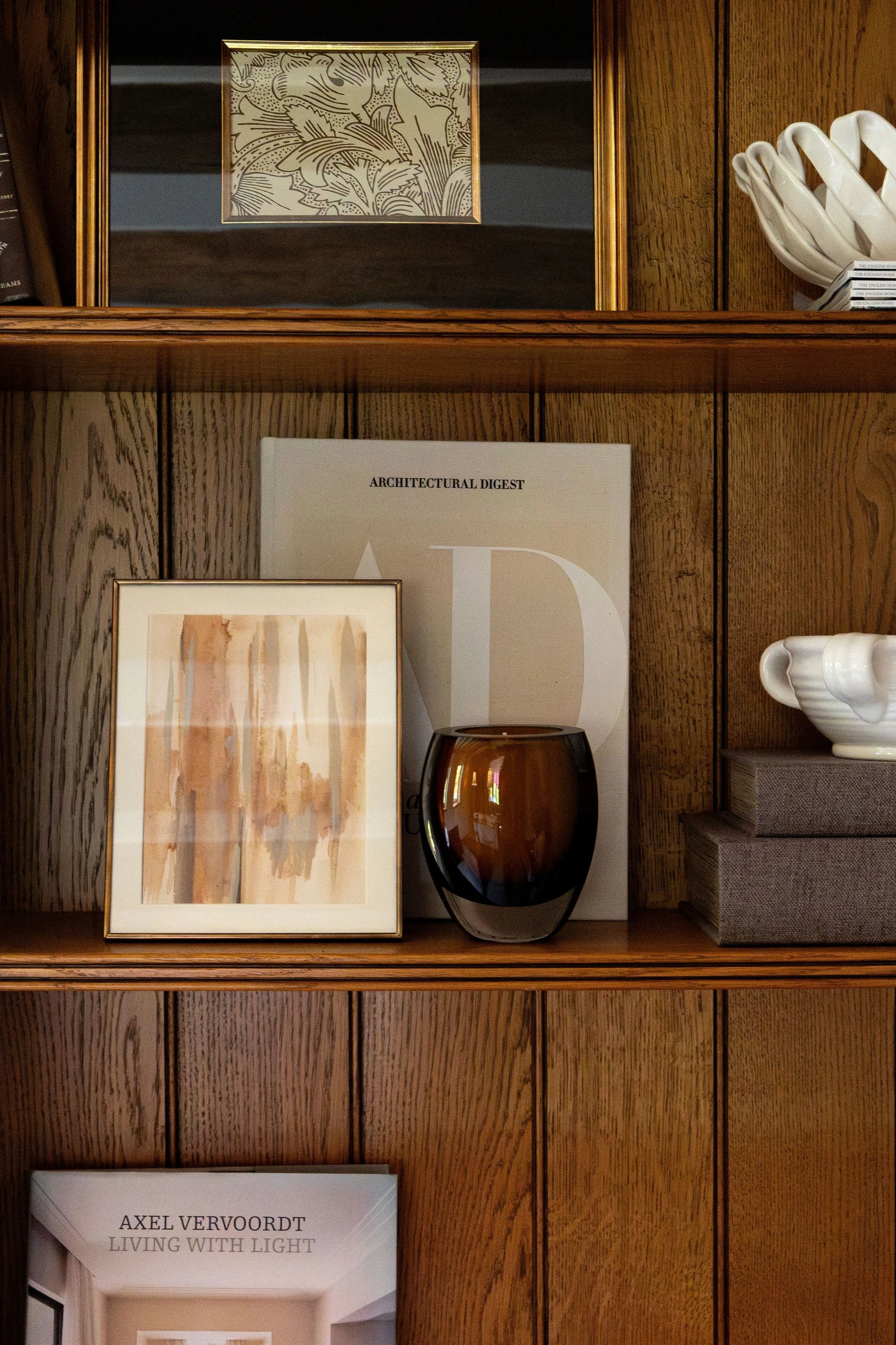 Bookshelf with framed artwork, a dark glass vase, a white ceramic bowl, and a book titled 'Living with Light' by Axel Vervoort.