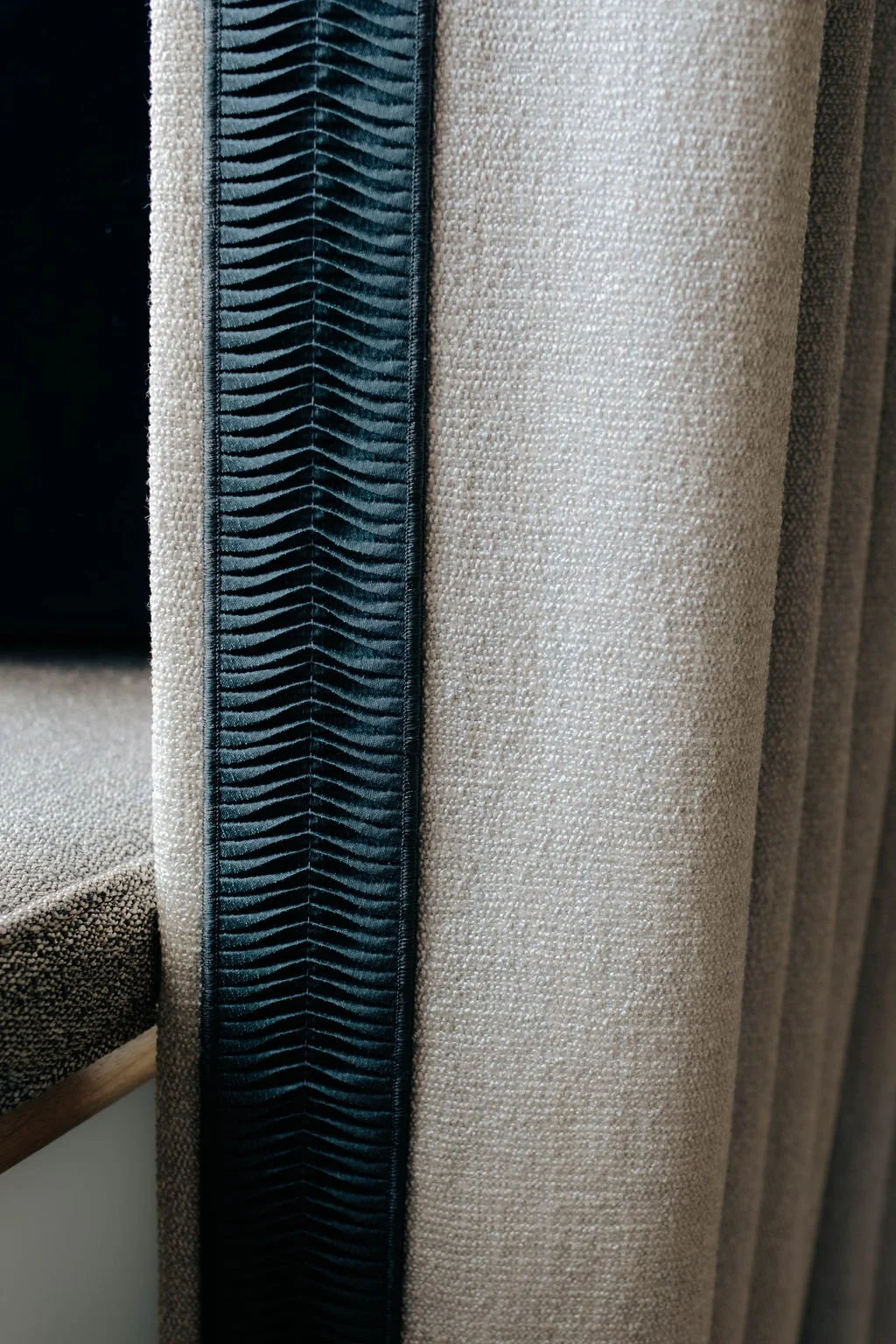 Close-up of beige upholstery fabric with a dark blue decorative trim featuring a zigzag pattern.