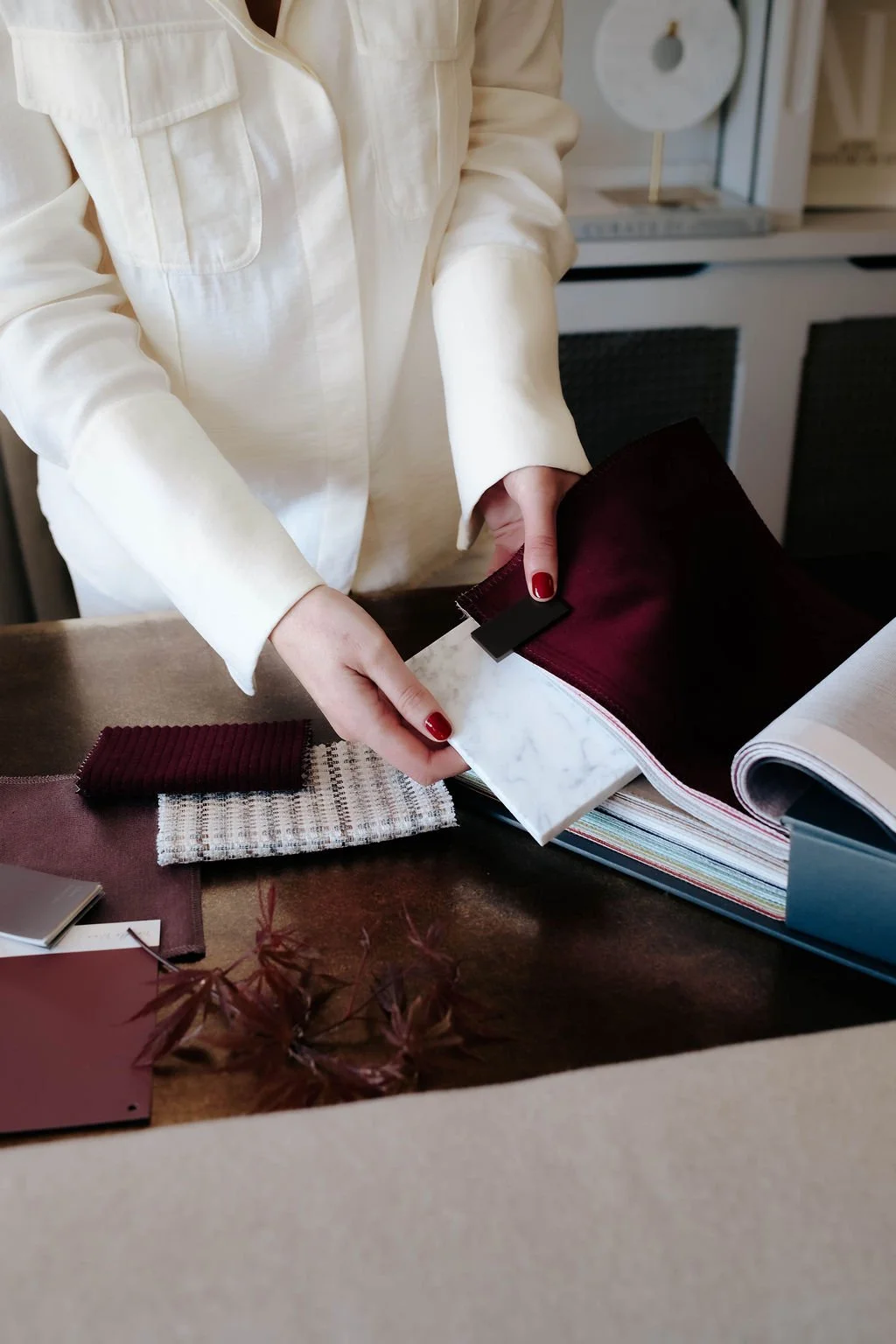 A person wearing a cream-colored jacket looking through fabric samples and color swatches on a table.