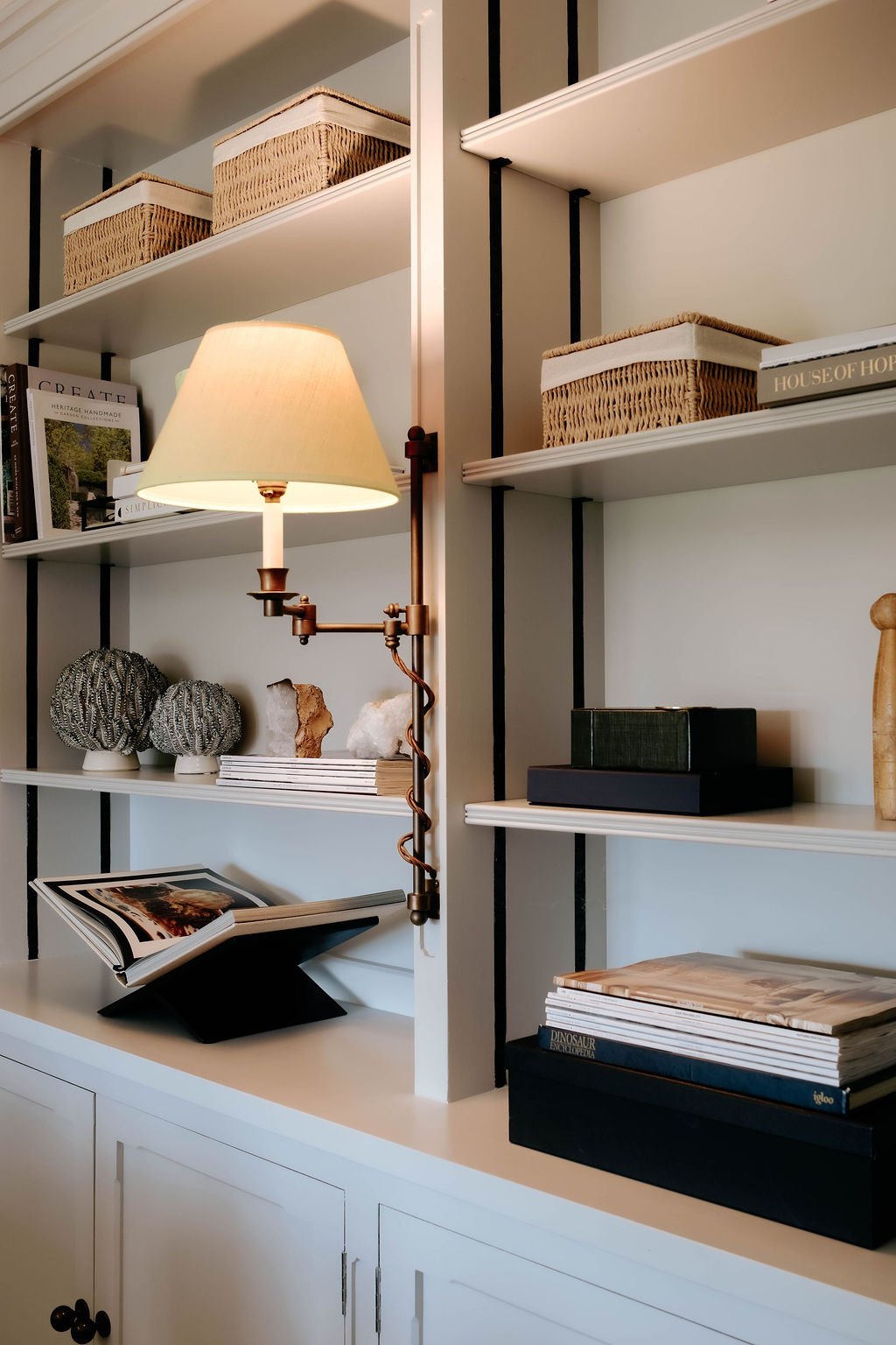 White bookshelf with decorative items, books, and a wall-mounted lamp with a beige lampshade.