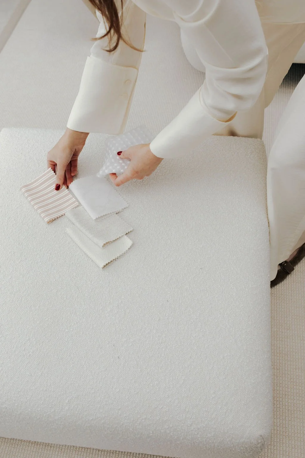Person arranging fabric sample swatches on a beige couch.
