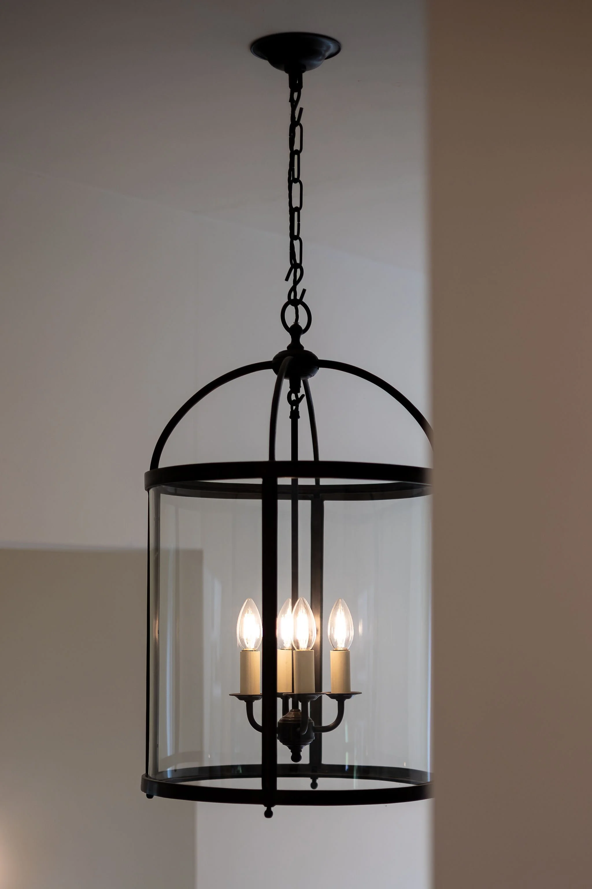 A black metal chandelier with five candle-shaped light bulbs, hanging from a chain attached to a ceiling.