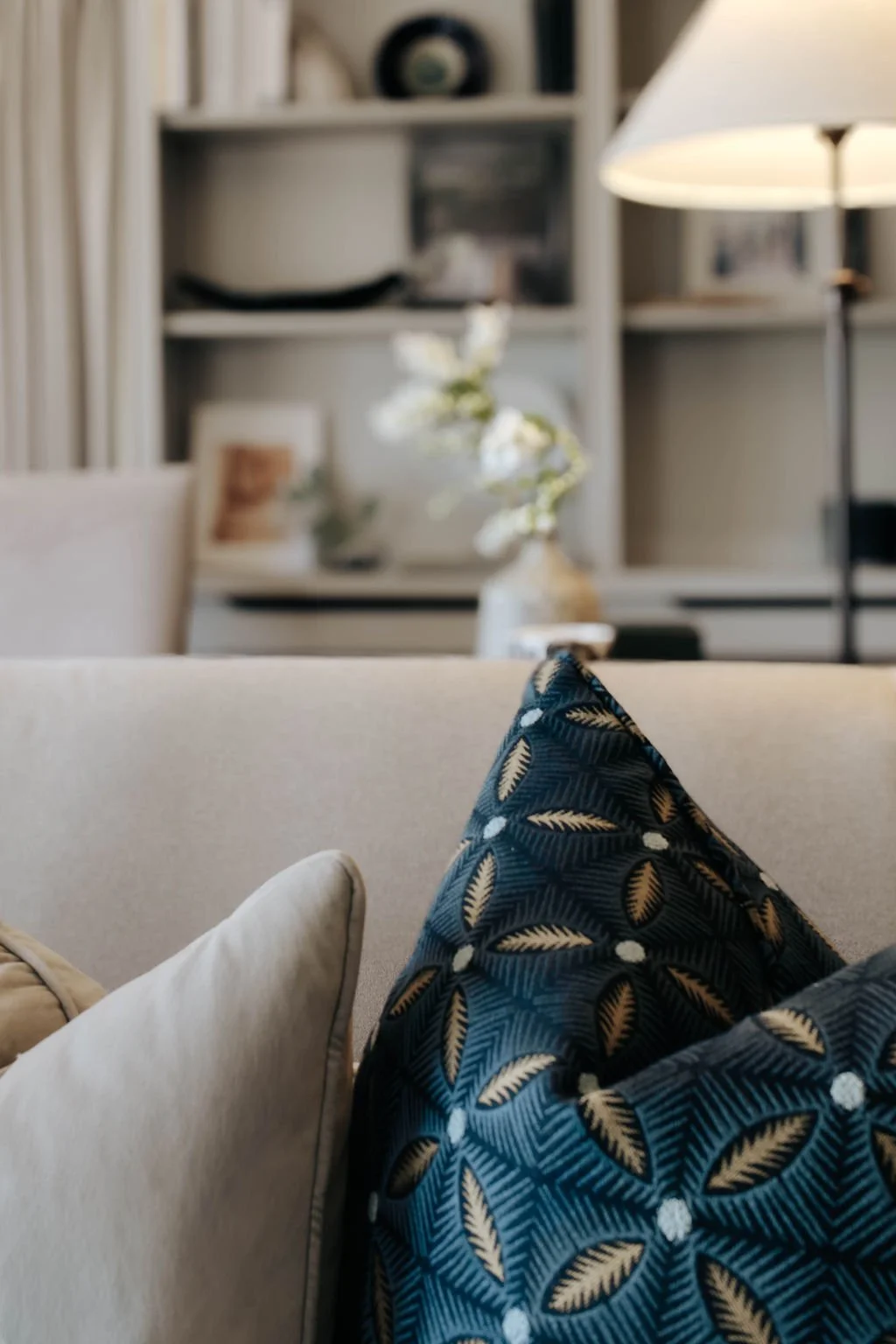 Close-up of a beige sofa with a decorative navy blue pillow featuring a leaf pattern, in a cozy living room.
