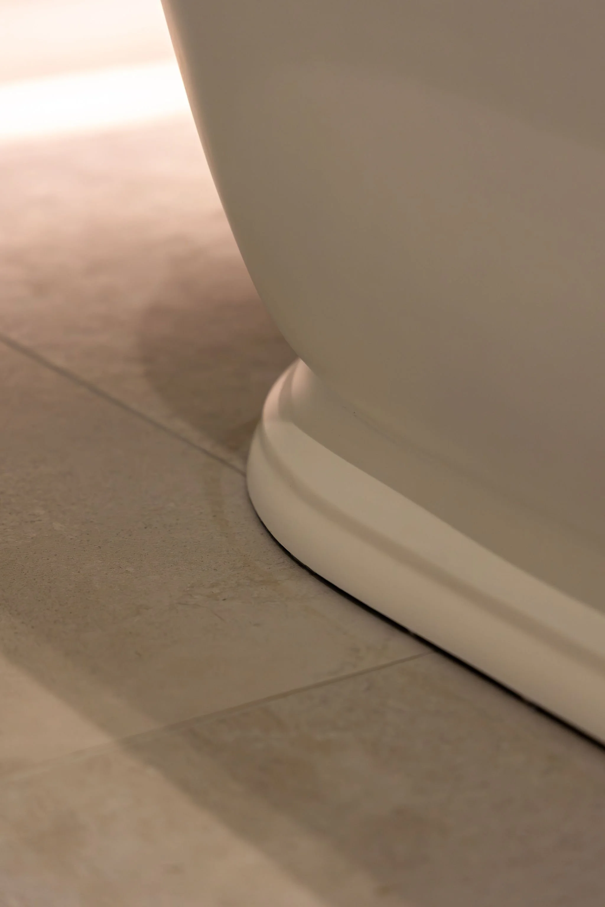 Close-up of a white toilet base on a tiled bathroom floor.