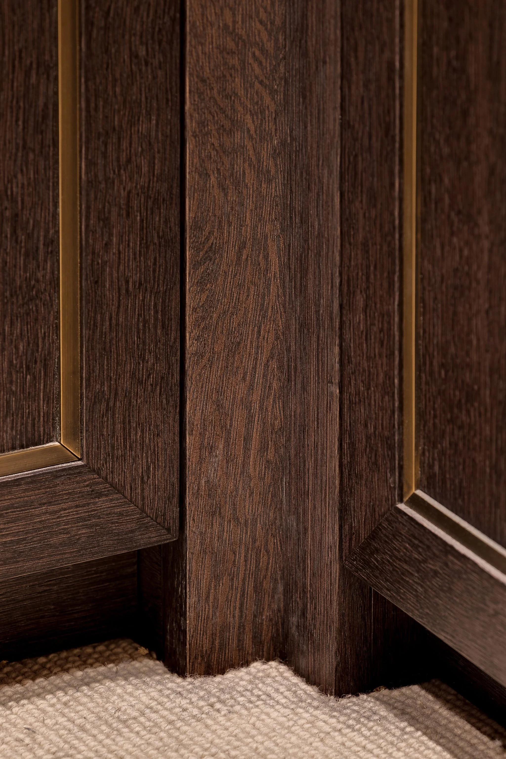 Close-up of the corner of a dark brown wooden cabinet with a textured finish, sitting on a beige carpet with a woven pattern.