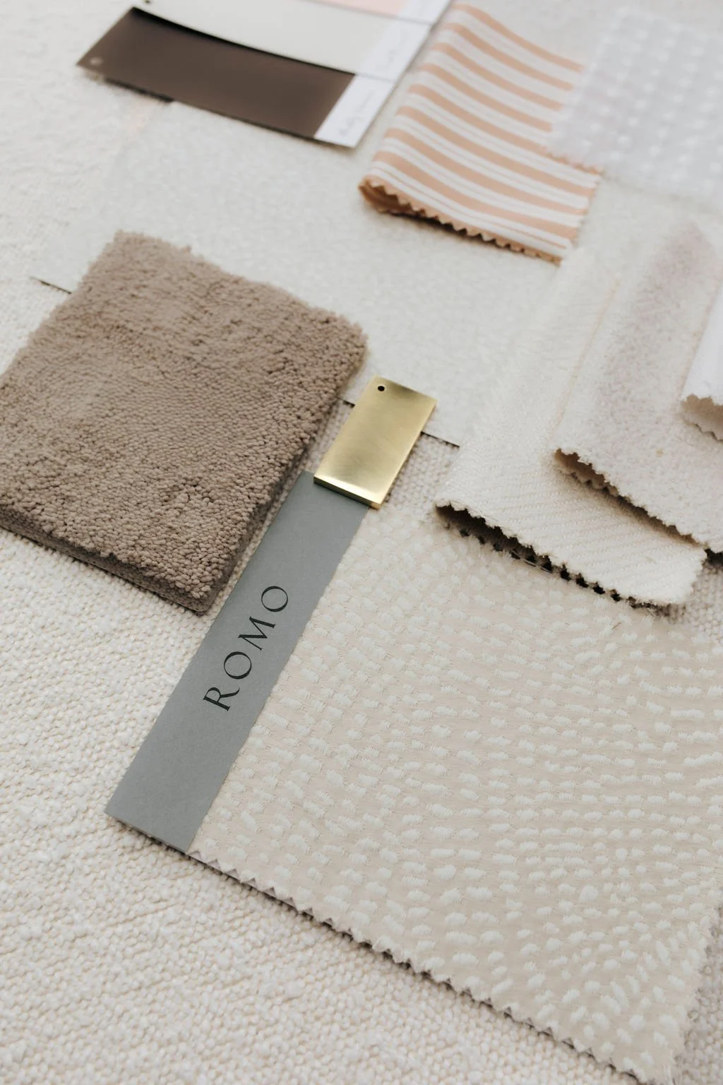Samples of beige and cream-colored fabrics, a small beige fabric swatch, a beige and pink striped fabric sample, a Gucci fabric sample, and a fabric color swatch labeled 'ROMO' on a textured beige background.