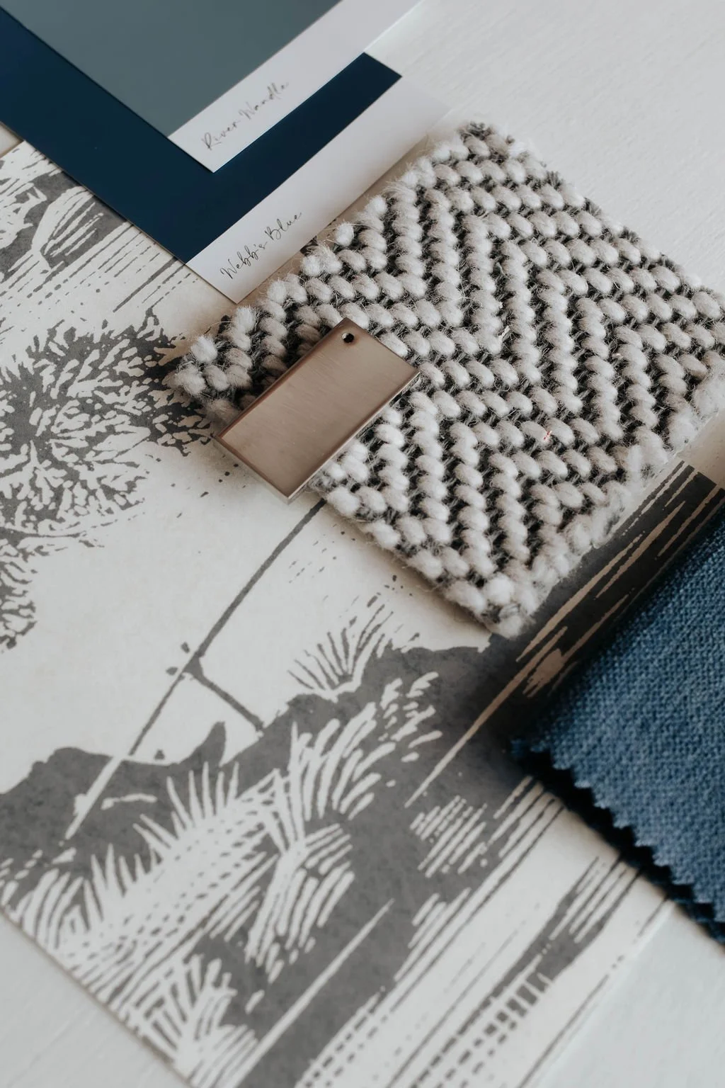 A flat lay photo of fabric swatches, color palette samples, and a textured black and white blanket on a patterned tabletop.