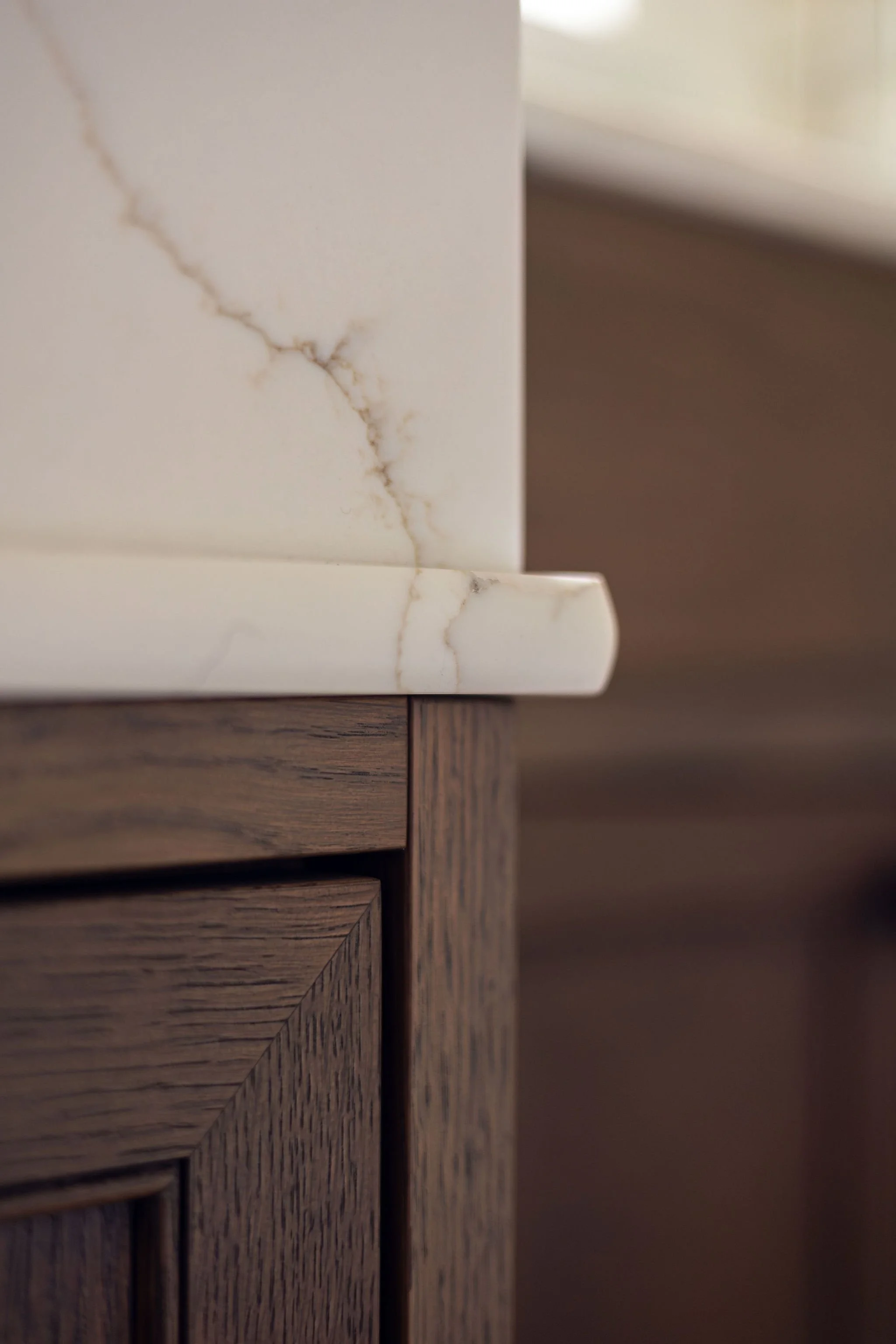 Close-up image of a corner where a white marble surface with veins meets a wooden cabinet with slatted doors.
