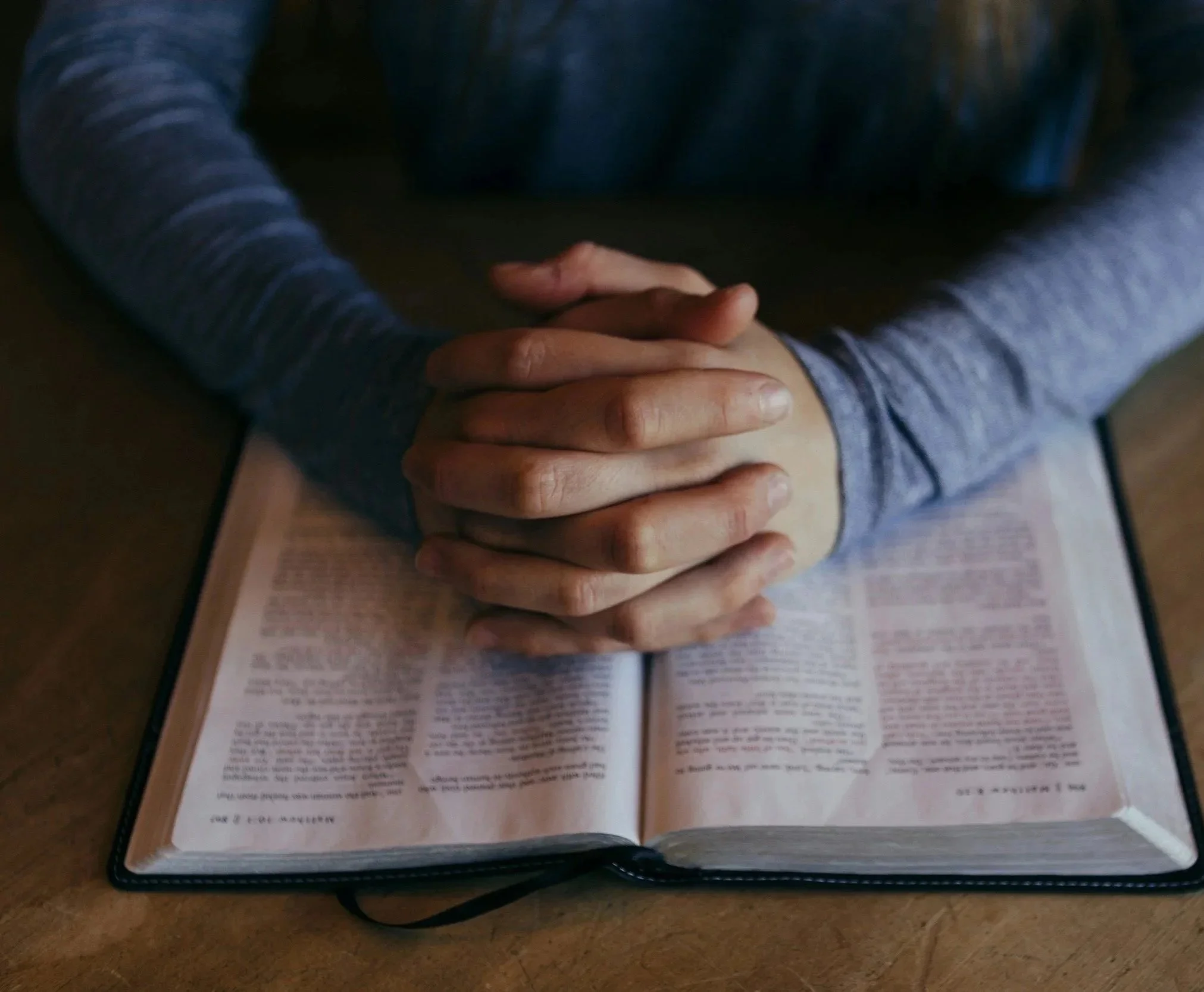 Close-up of two people holding hands over an open book or magazine on a table.