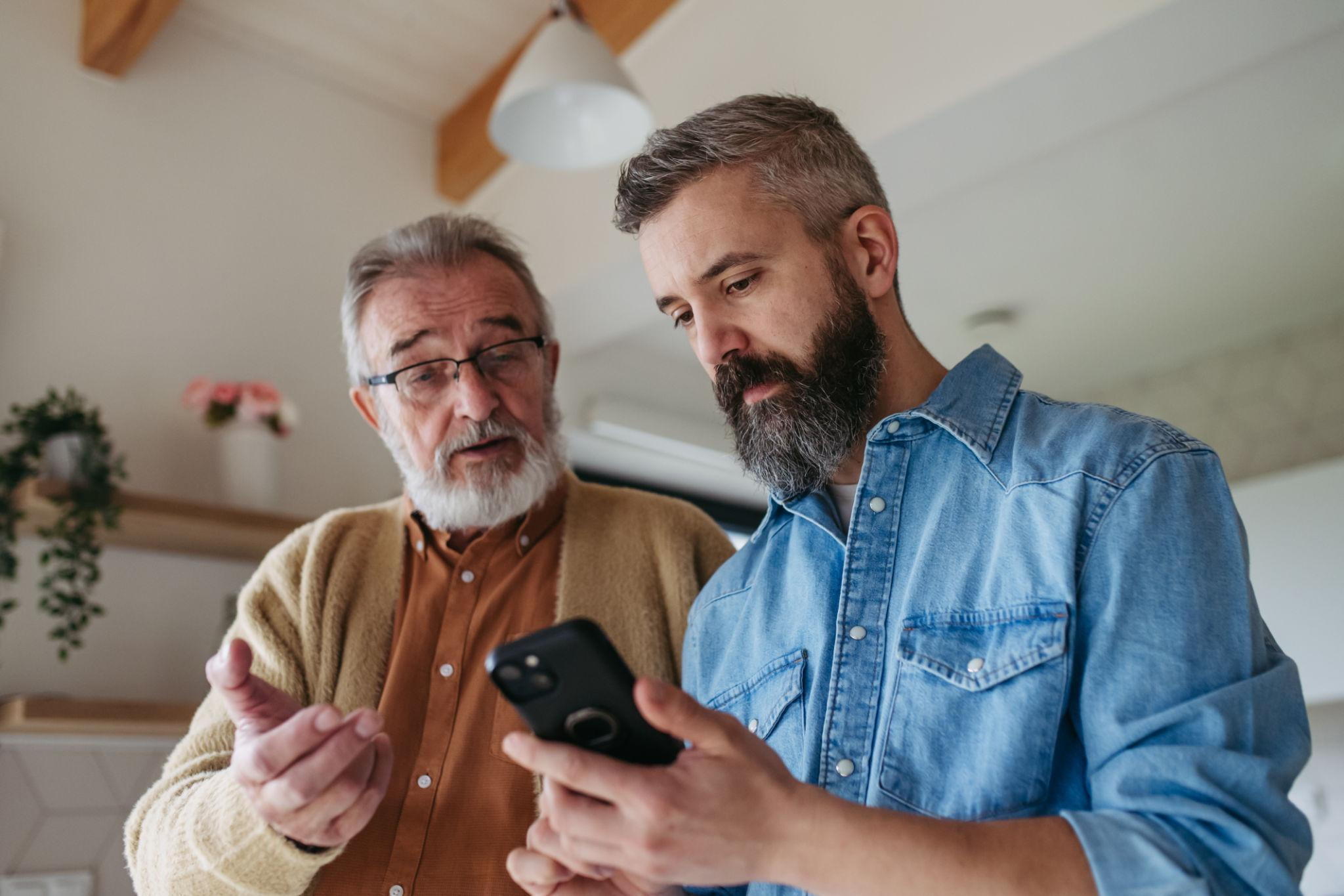 Twee mannen die samen een smartphone bekijken in een huiselijke omgeving.