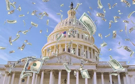Hundred-dollar bills flying in the air above the U.S. Capitol building against a clear blue sky.