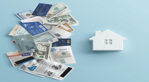 Assorted credit cards, cash, and utility bills on a light blue surface with a small white house model.