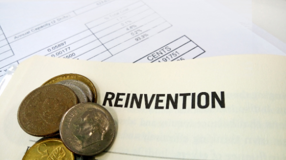 Close-up of coins and a financial document placed on a book titled 'Reinvention'.