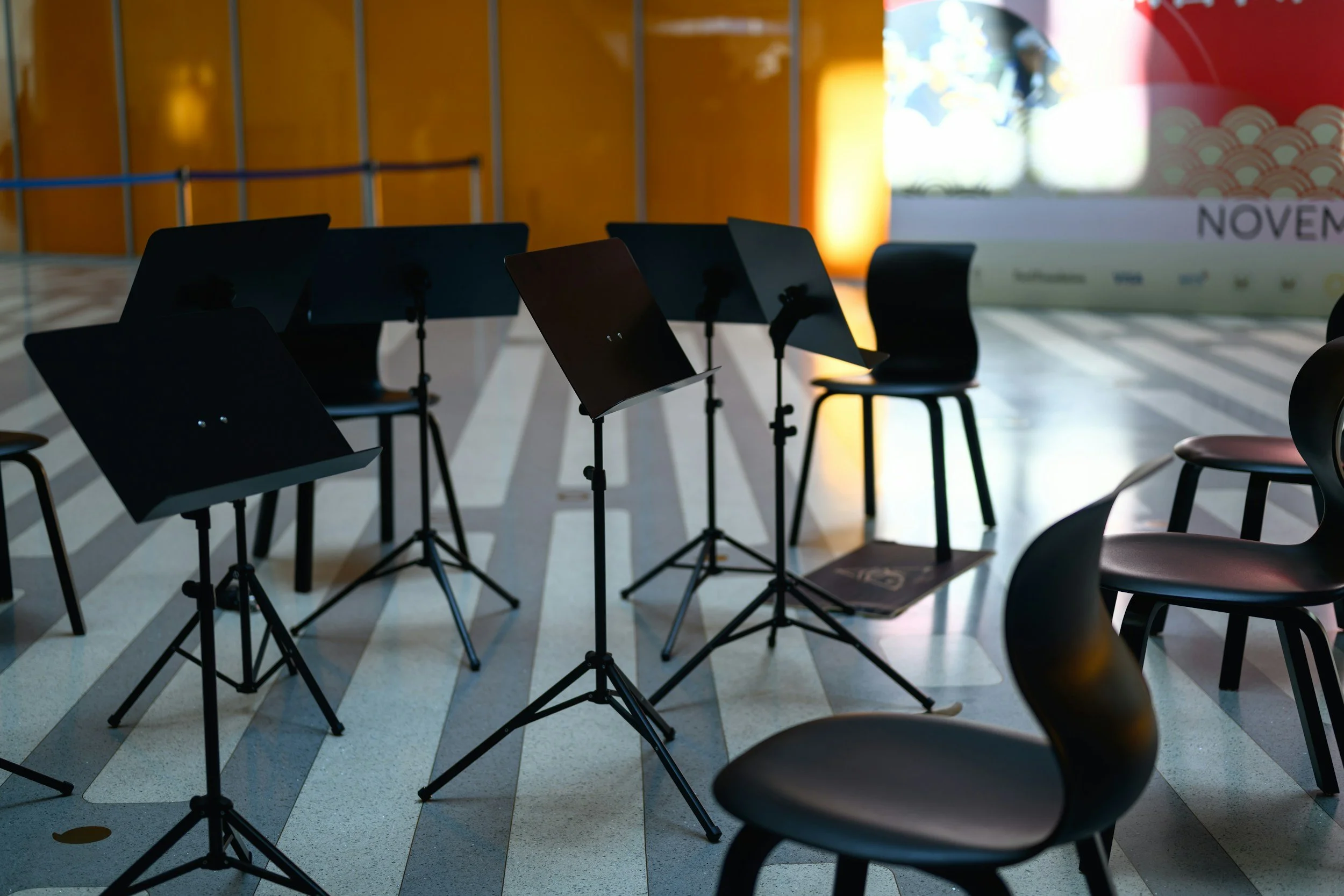 Empty chairs with music stands in a dimly lit venue, likely for a musical performance.
