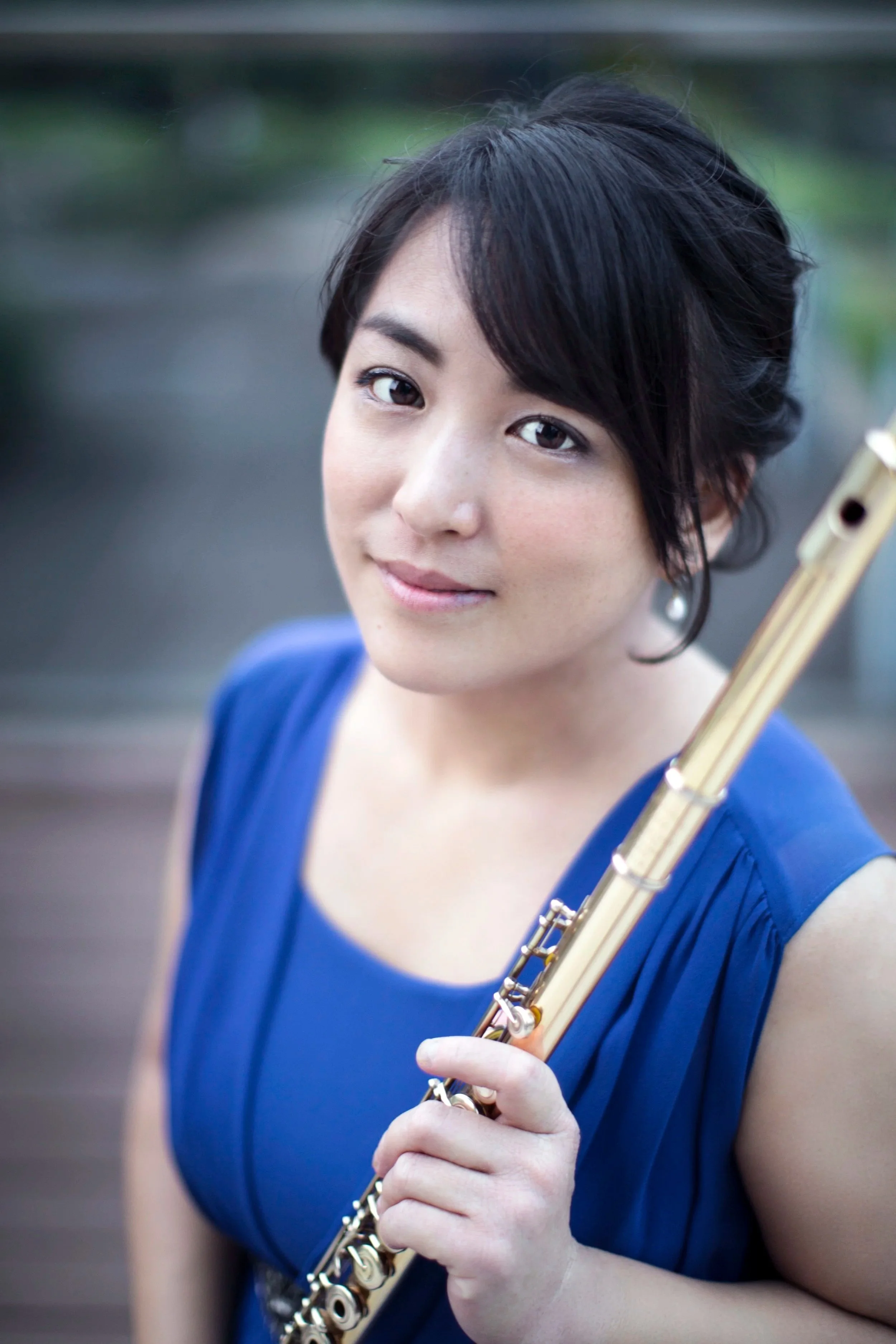 A woman with short black hair wearing a blue dress holding a flute.