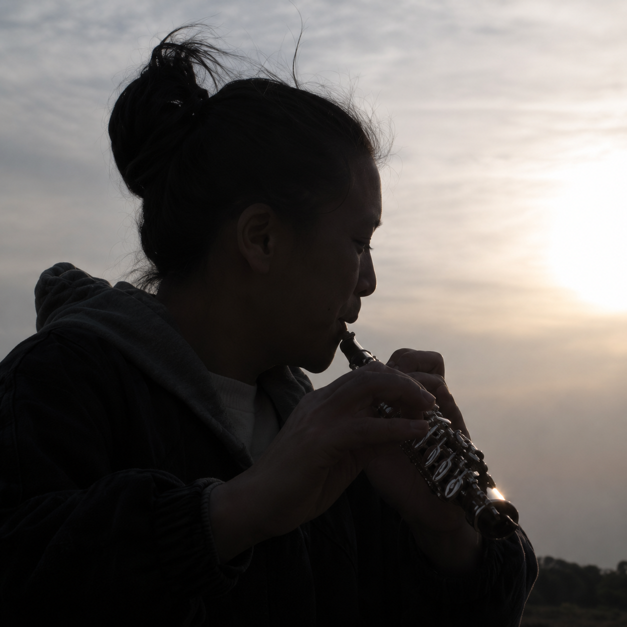 Silhouette of a person playing a wind instrument outdoors at sunset or sunrise.