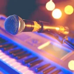 Close-up of a microphone angled toward a keyboard, illuminated by warm stage lights. The scene suggests a live music setup, evoking a vibrant and energetic atmosphere.