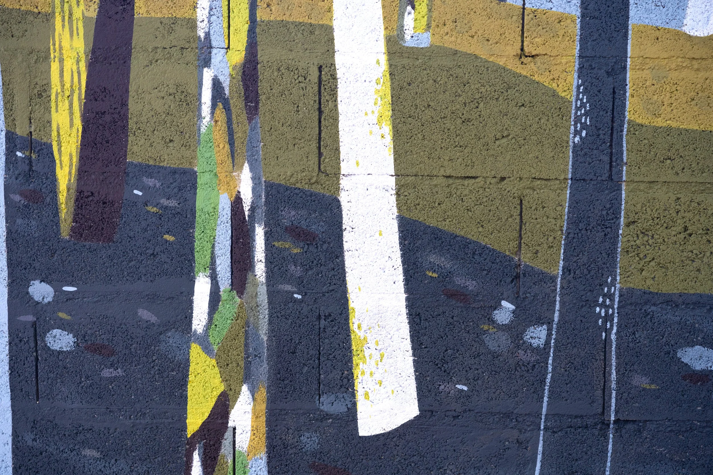 Une peinture de rue représentant des lignes blanches, jaunes et vertes sur un mur en béton noir, avec des éclaboussures de peinture blanche.