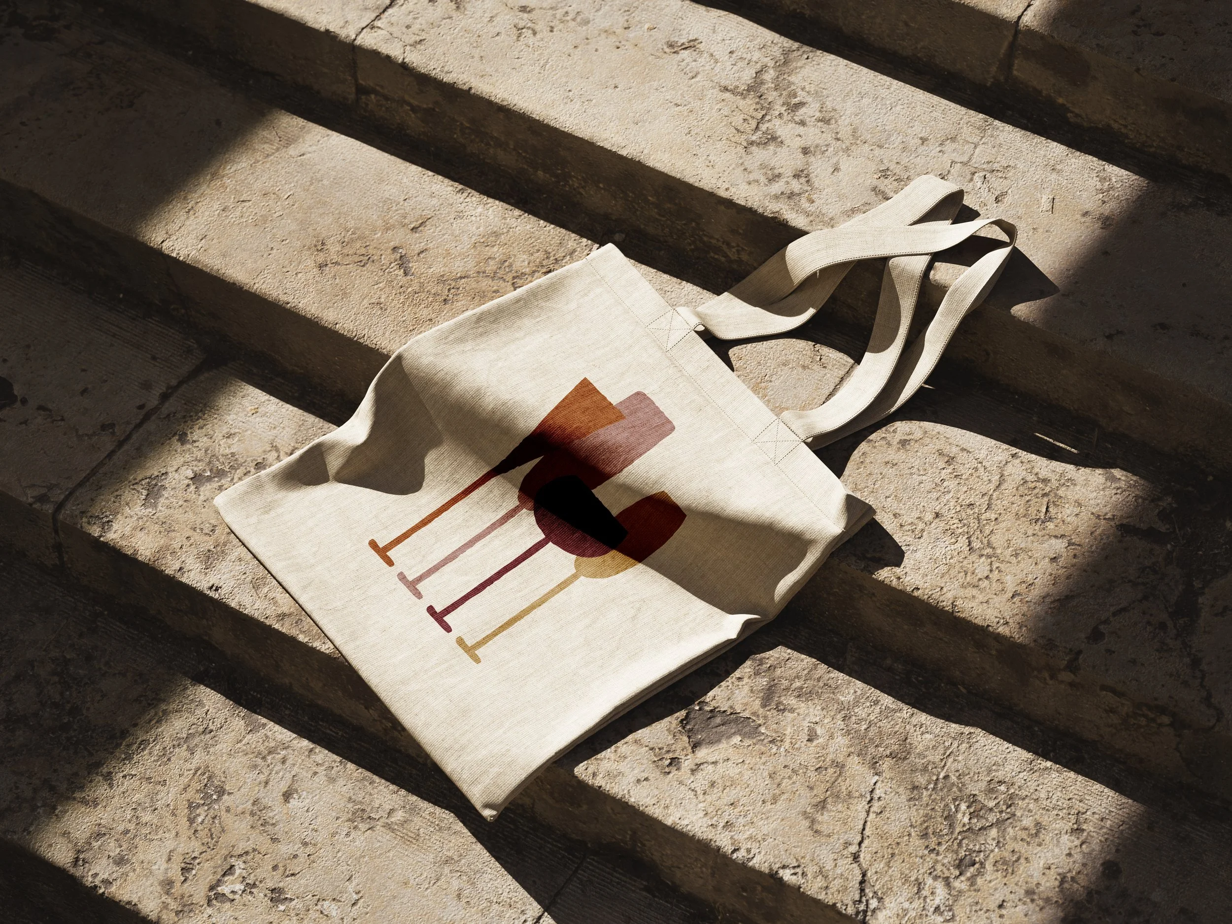 Sac en toile beige avec un motif coloré posé sur des escaliers en pierre.