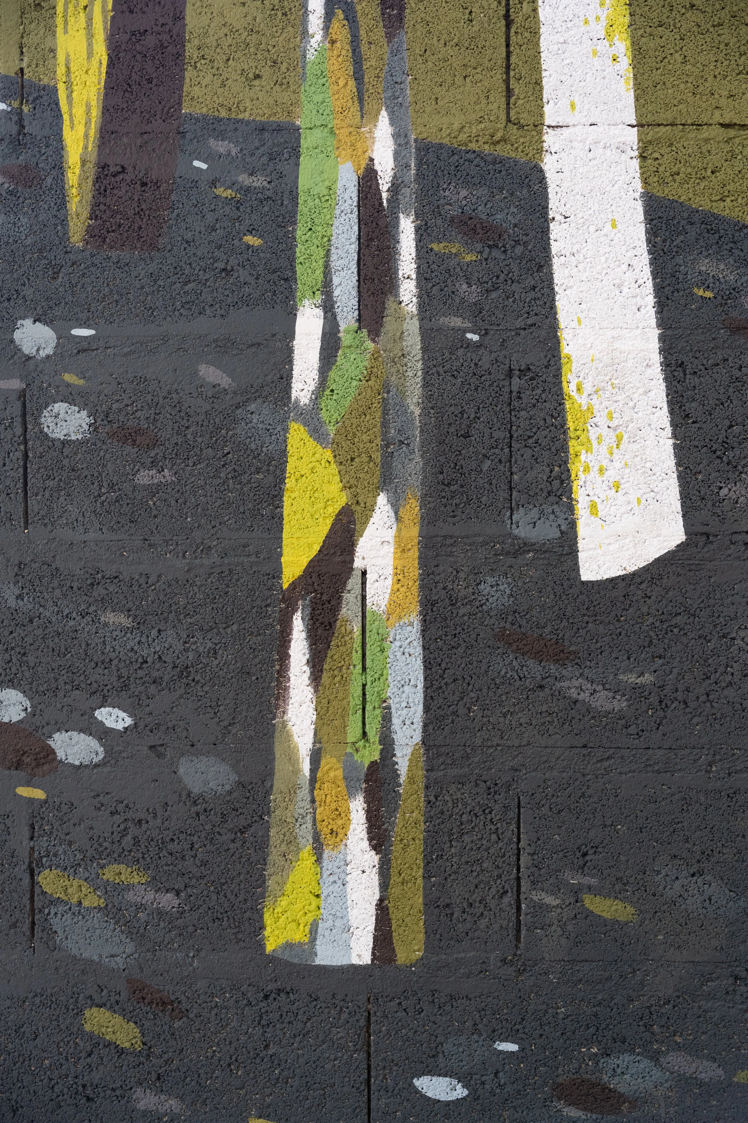 Peinture urbaine sur un sol en béton avec lignes blanches, vertes, jaunes, et dessins abstraits, notamment des formes en fil de fer ou en cercle.